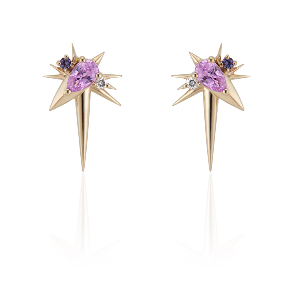   Front view of slanted drop earrings, each with 1 pear-shaped pink sapphire, set at 45-degree angle, flanked by small round diamonds and sapphires. 9 yellow gold spikes of varying lengths extend from the oval setting, with a larger and longer spike pointed down. 