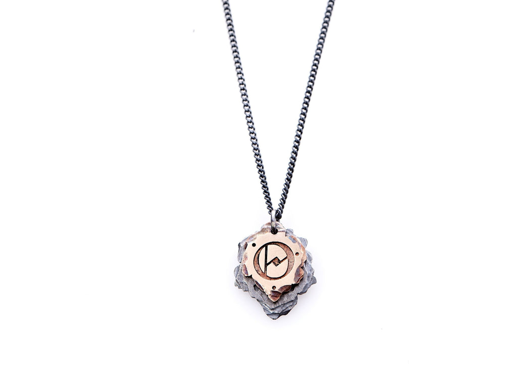 Hand crafted, customizable Initial Necklace with 2 jagged-edged plates hanging from an oxidized sterling silver curbed chain. Top plate is hand forged rose gold with a custom engraving of the letter "O" in Old English lettering with 2 hand engraved dots on either side. Bottom plate is hand forged oxidized sterling silver and slightly larger than the rose gold plate. The top plate partially covers the bottom plate, and edges of cross- bones are visible on the bottom plate.