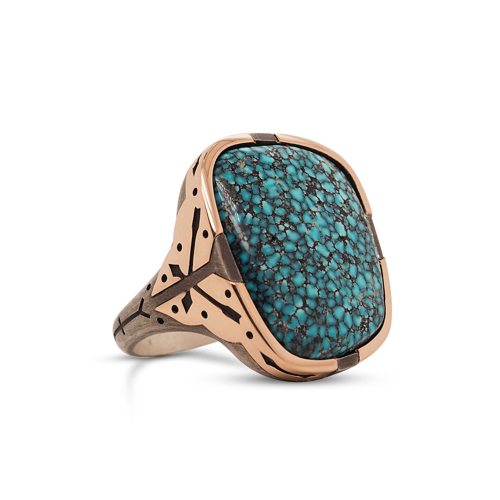  Partial side view of bespoke men’s black-webbed Kingman Turquoise Ring with a rounded square head tapering to a thin metal band. Turquoise stone has slight polished shine and black webbing. The head of the ring’s oxidized silver band is accented by 4 separate rose gold pieces at each corner, leaving small tabs of silver visible on all 4 sides of the head. A narrow stretch of sterling silver continues between the edges of the rose gold accents to a flared tab at the head.