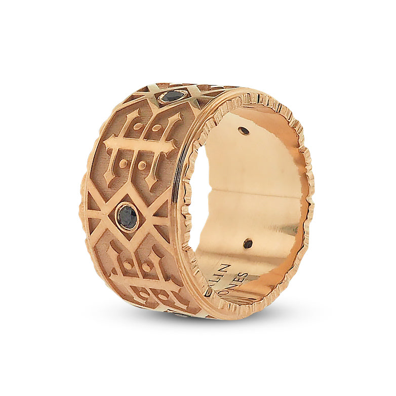 Front side angle of black diamond men’s wedding band. Polished rose gold detailing features alternating navajo-style designs; a grid of double-sided arrows with dots, and 2 rows of side-by-side zig-zag lines with centered round black diamond.
