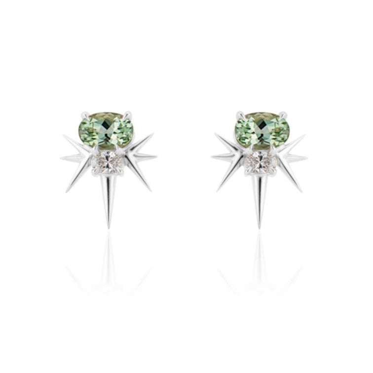 Front view of white gold spike earrings, each featuring 1 horizontal oval-shaped green tourmaline stone with 1 oval-shaped diamond below. 7 yellow gold spikes extend out from the diamond, 3 on either side and 1 slightly longer spike pointed down. 
