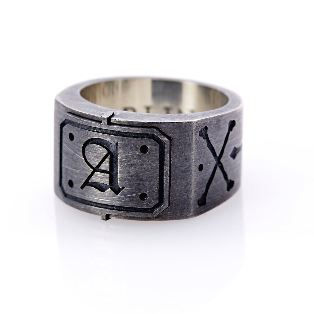  Oxidized sterling silver men’s signet ring with a thick flat band hand-crafted in New York. Semi-raised octagonal engraved top cap with a customizable insignia design of an engraved letter “A” in Old English Style lettering and 4 engraved dots at each corner. The initial on the ring is surrounded by a bold black engraved border that follows the inside edge of the rectangle. The rectangle’s top and bottom edge is accented by a small lip in the center that wraps around the corner edge of the ring.