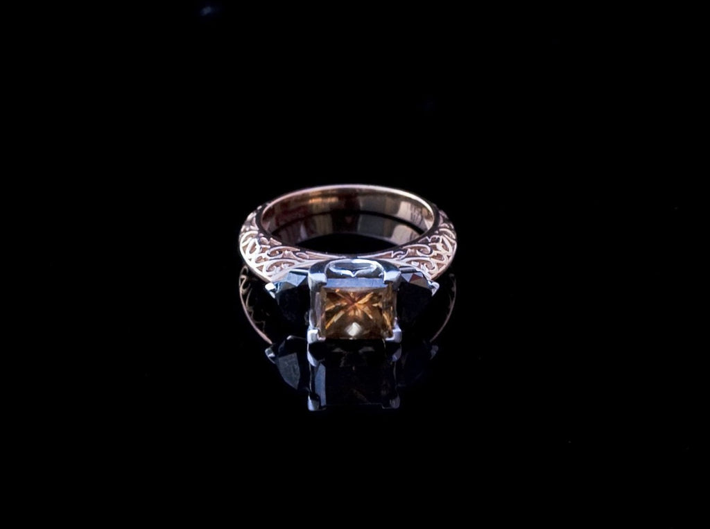 Overhead view of the White Gold Cognac Diamond Ring, with the head of the ring pointed towards camera. Cushion cut cognac diamond held in the center with 2 shield cut black diamonds on either side.