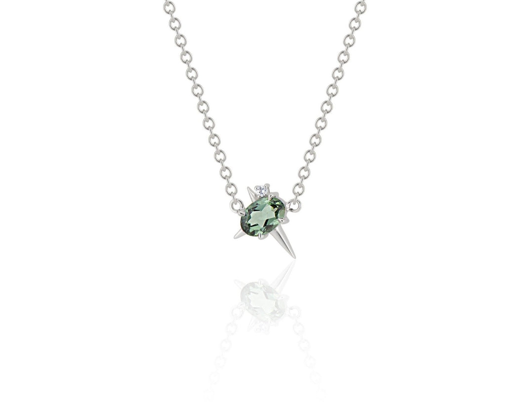  Front view of pendant necklace featuring an oval-shaped green tourmaline gemstone with small round diamond fixed to a white gold round-link chain. 2 short spikes extend from top and side with a larger spike angled down, creating an angled crucifix.