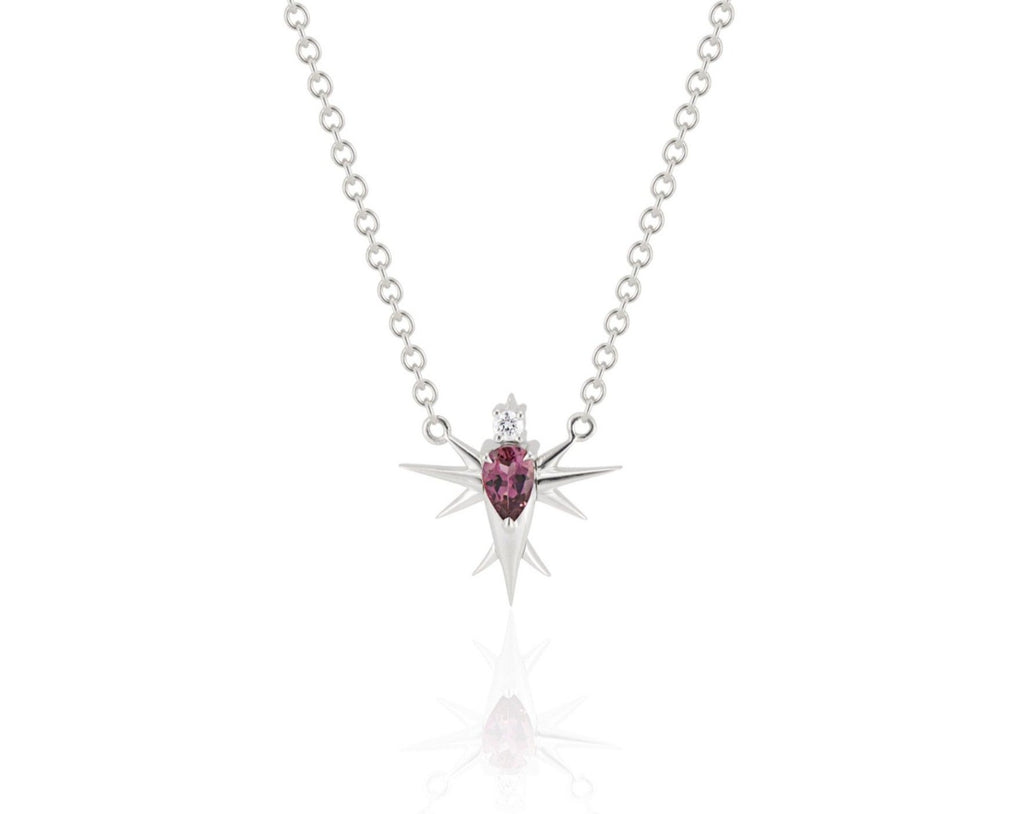 Front view of abstract bird necklace connected to a white gold round-link chain. A pear-shaped pink tourmaline stone forms the bird’s body, topped with a round diamond head. White gold spikes extend from the body to form wings and a tail. 
