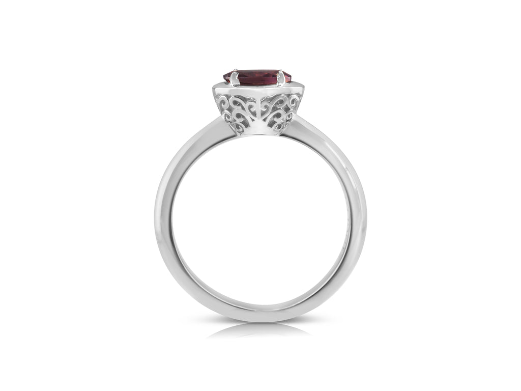 Side view of filigree ring with distinctive white gold basket. The filigree is a mirrored swirling pattern that reaches up and out from the base of the basket at the bridge. The pink tourmaline stone lays flat, slightly raised above the basket.