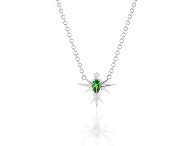 Front view of abstract bird pendant necklace connected to a white gold round-link chain. A pear-shaped tsavorite stone forms the bird’s body, topped with a round diamond head. White gold spikes extend from the body to form wings and a tail. 