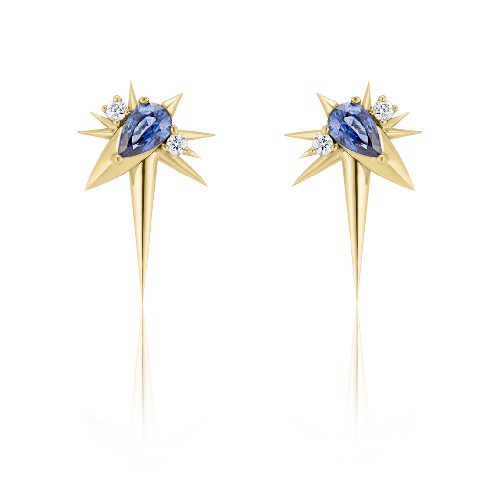 Front view of slanted sapphire drop earrings, each with 1 pear-shaped blue sapphire, set at 45-degree angle, flanked by small round diamonds. 9 yellow gold spikes of varying lengths extend from the oval setting, with a larger and longer spike pointed down.