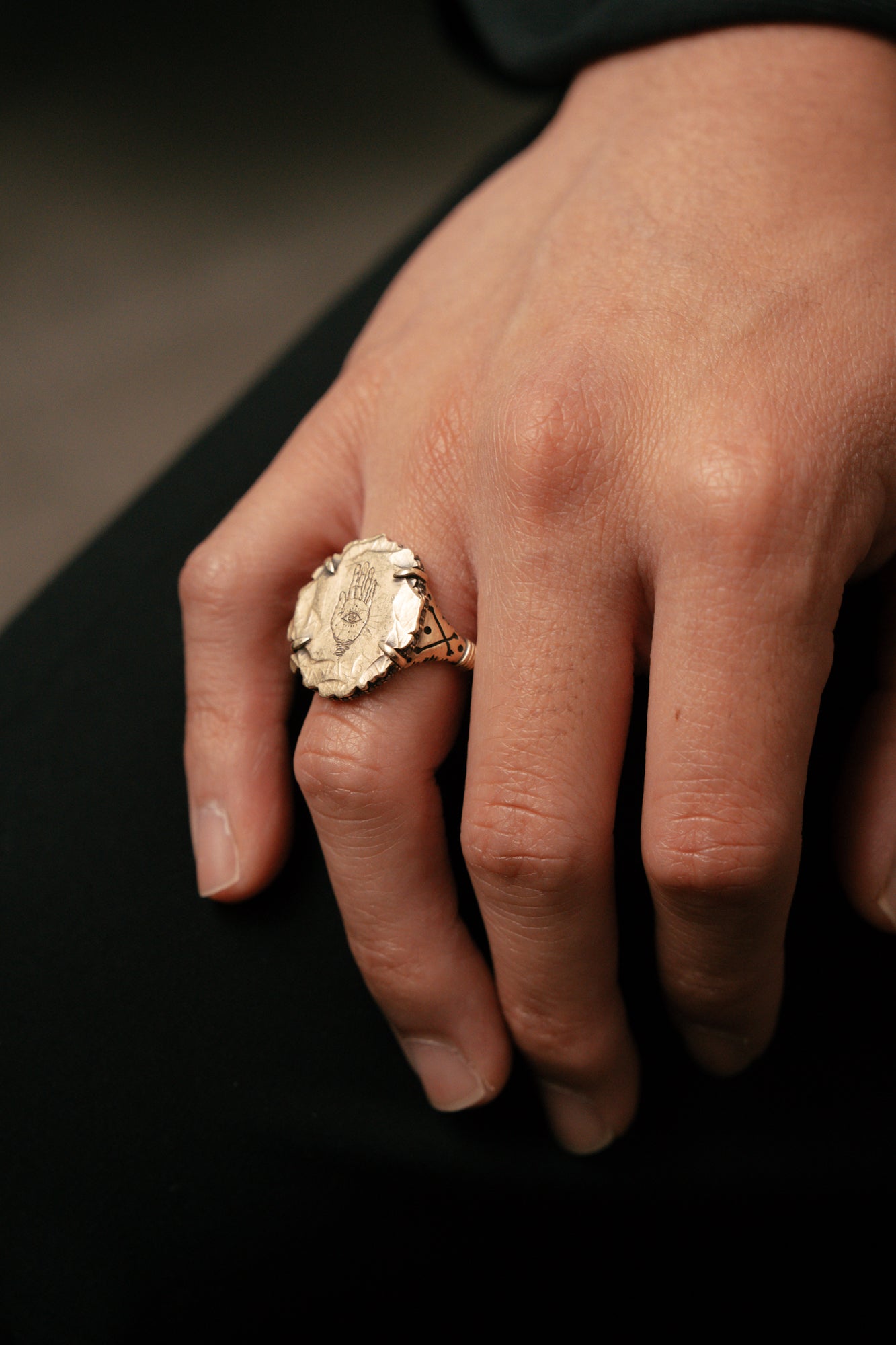 Close-up of a hand wearing a gold ring on a dark background