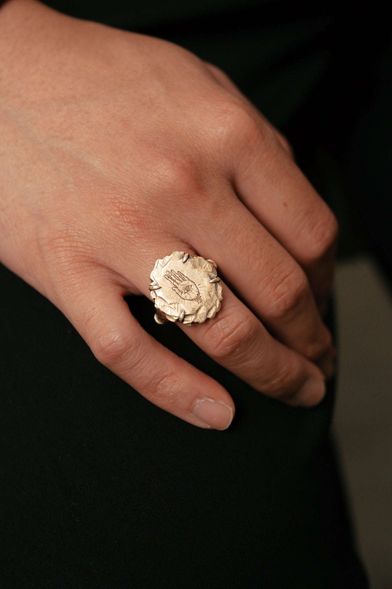 Hand wearing a gold ring with intricate design on a dark background