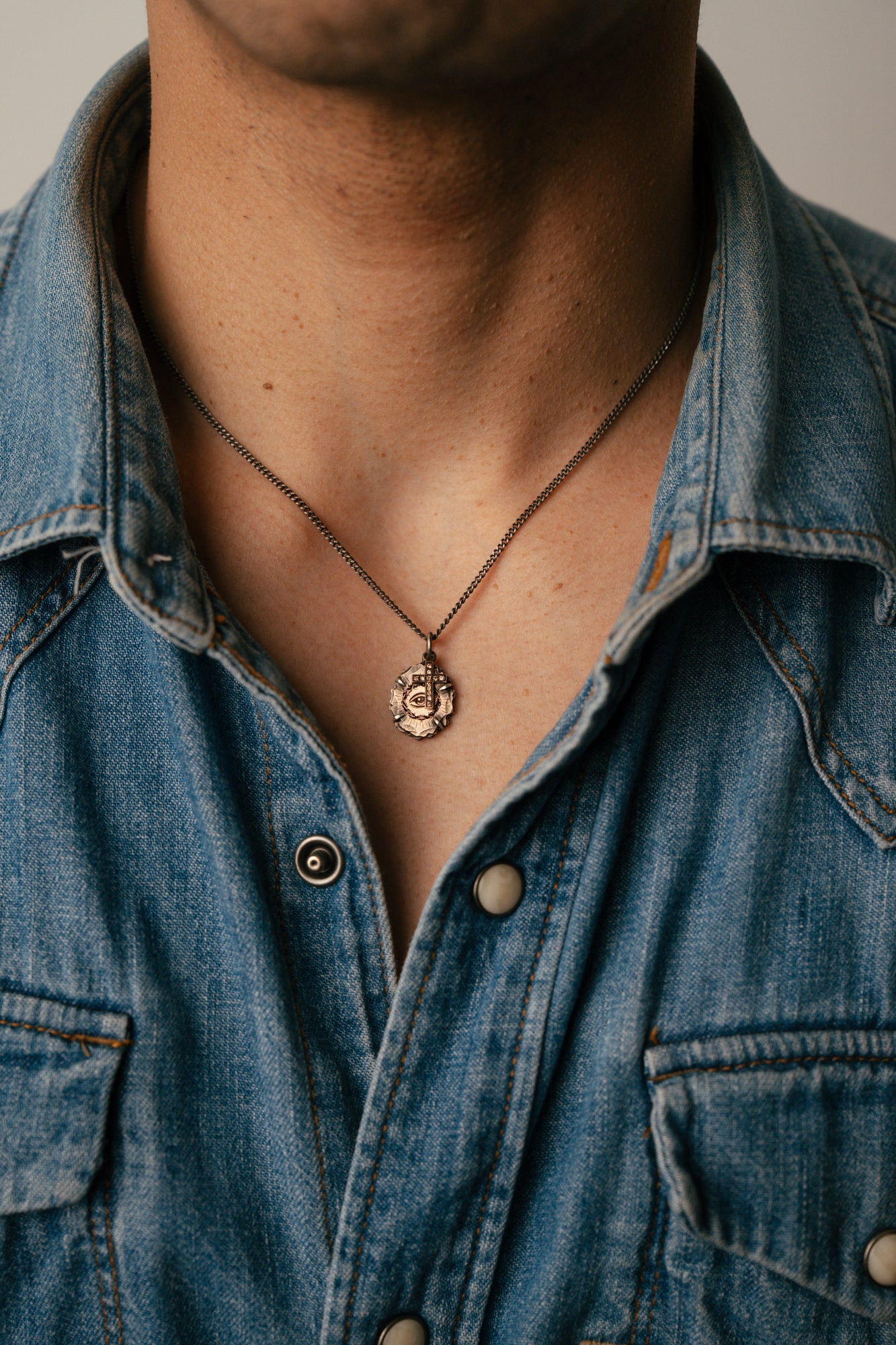 Person wearing a blue denim shirt with a necklace featuring a pendant.