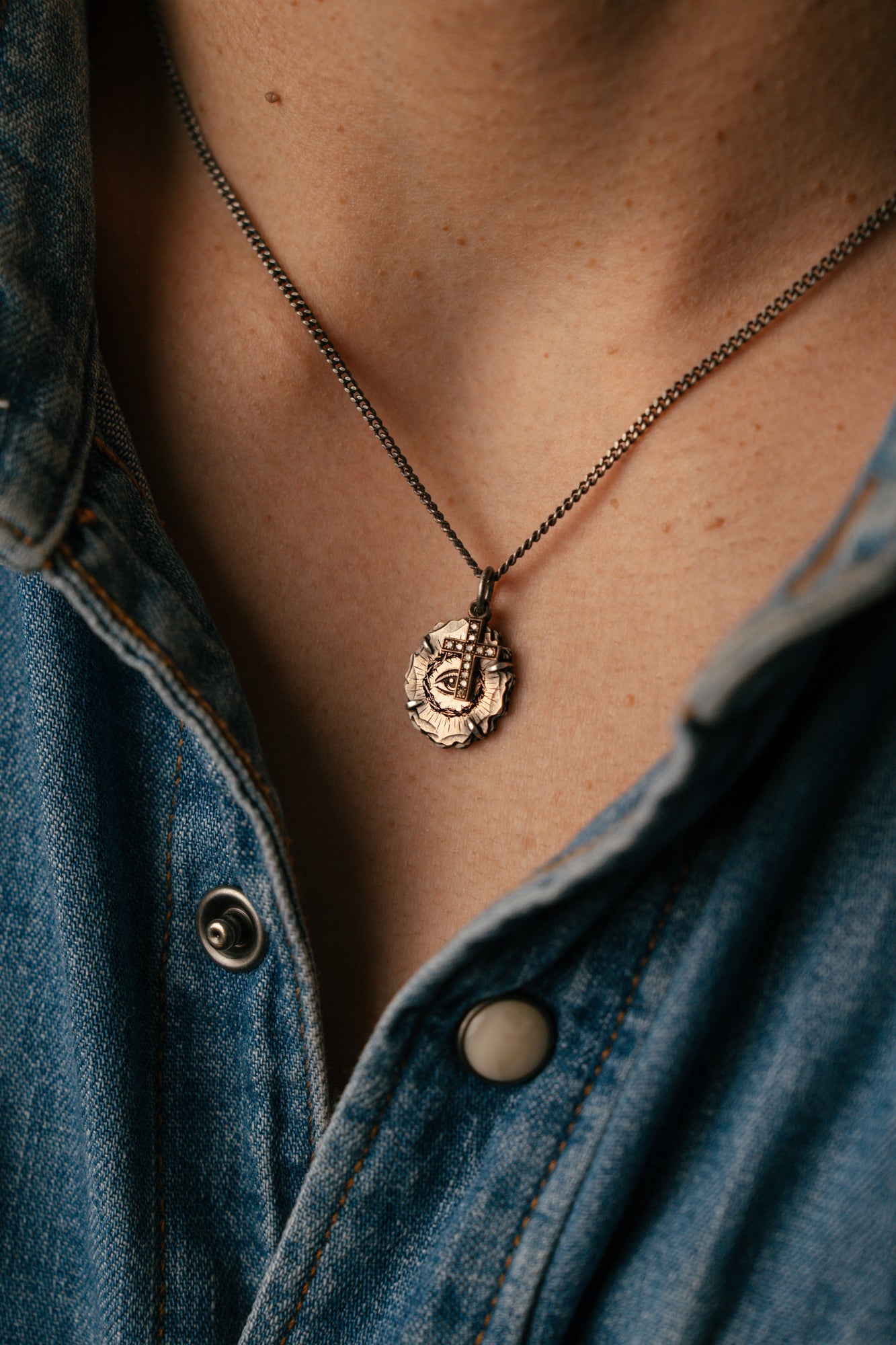 Necklace with a pendant worn by a person wearing a denim jacket.
