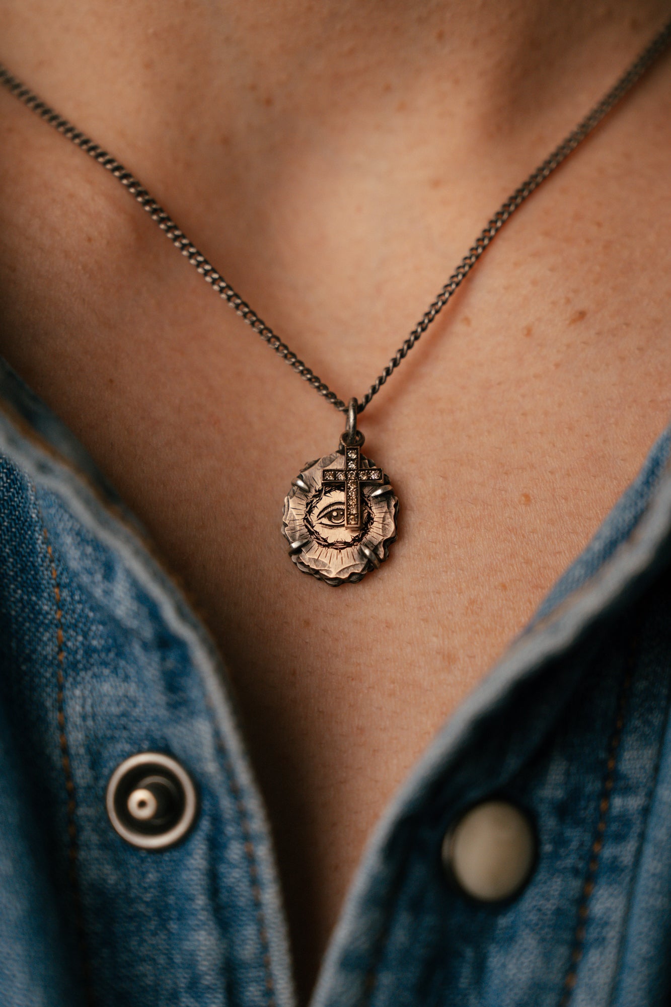 Close-up of a necklace with a pendant on a person wearing a denim jacket.
