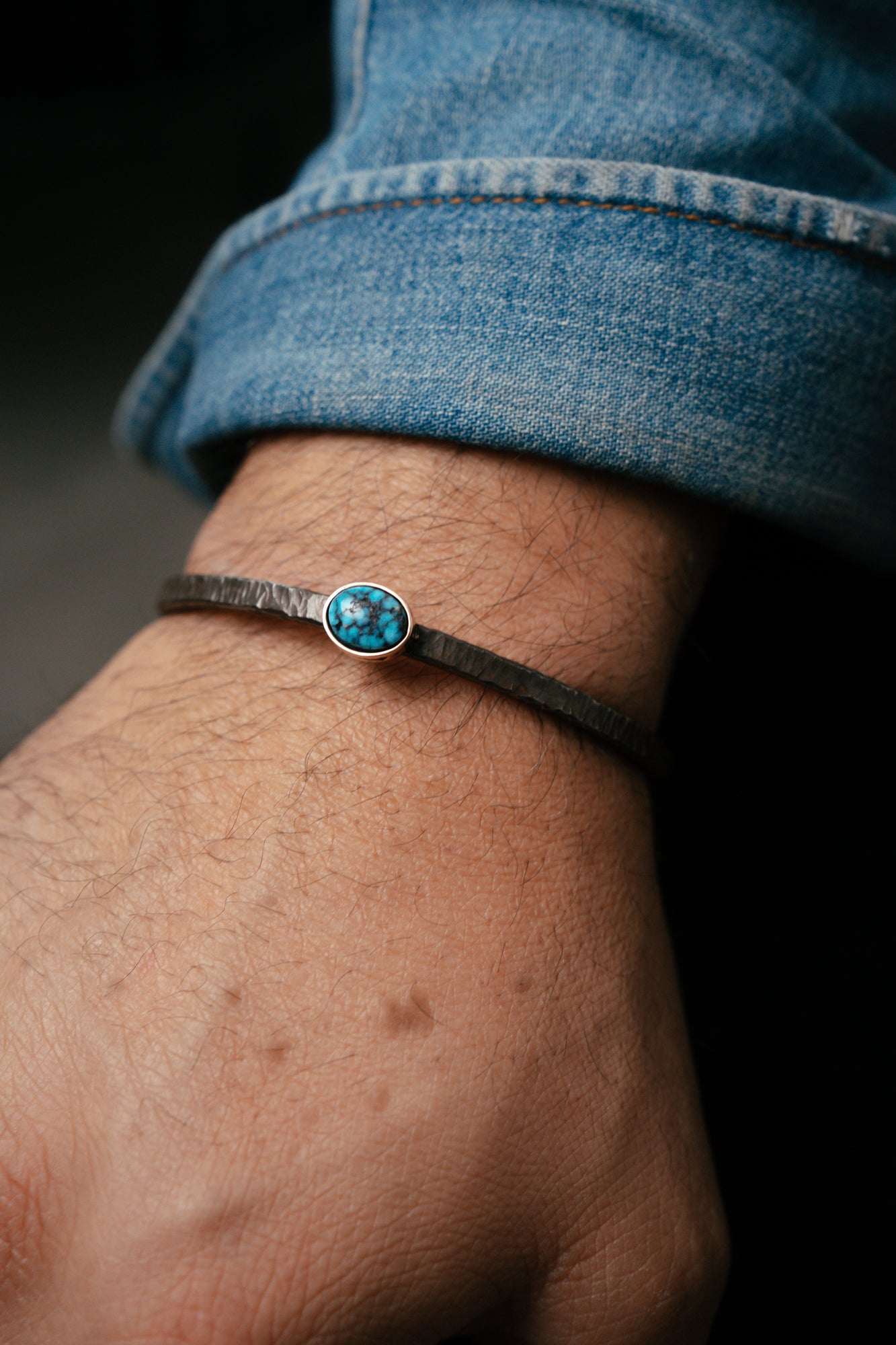 Close-up of a wrist wearing a bracelet with a blue gemstone against a dark background