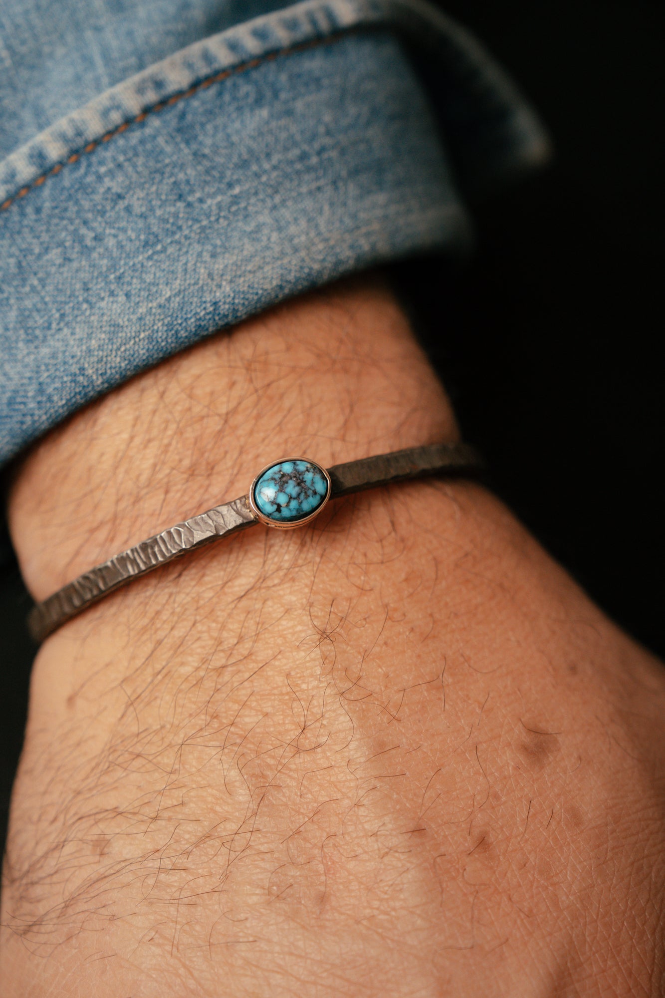 Bracelet with a turquoise stone on a wrist, wearing a denim shirt.