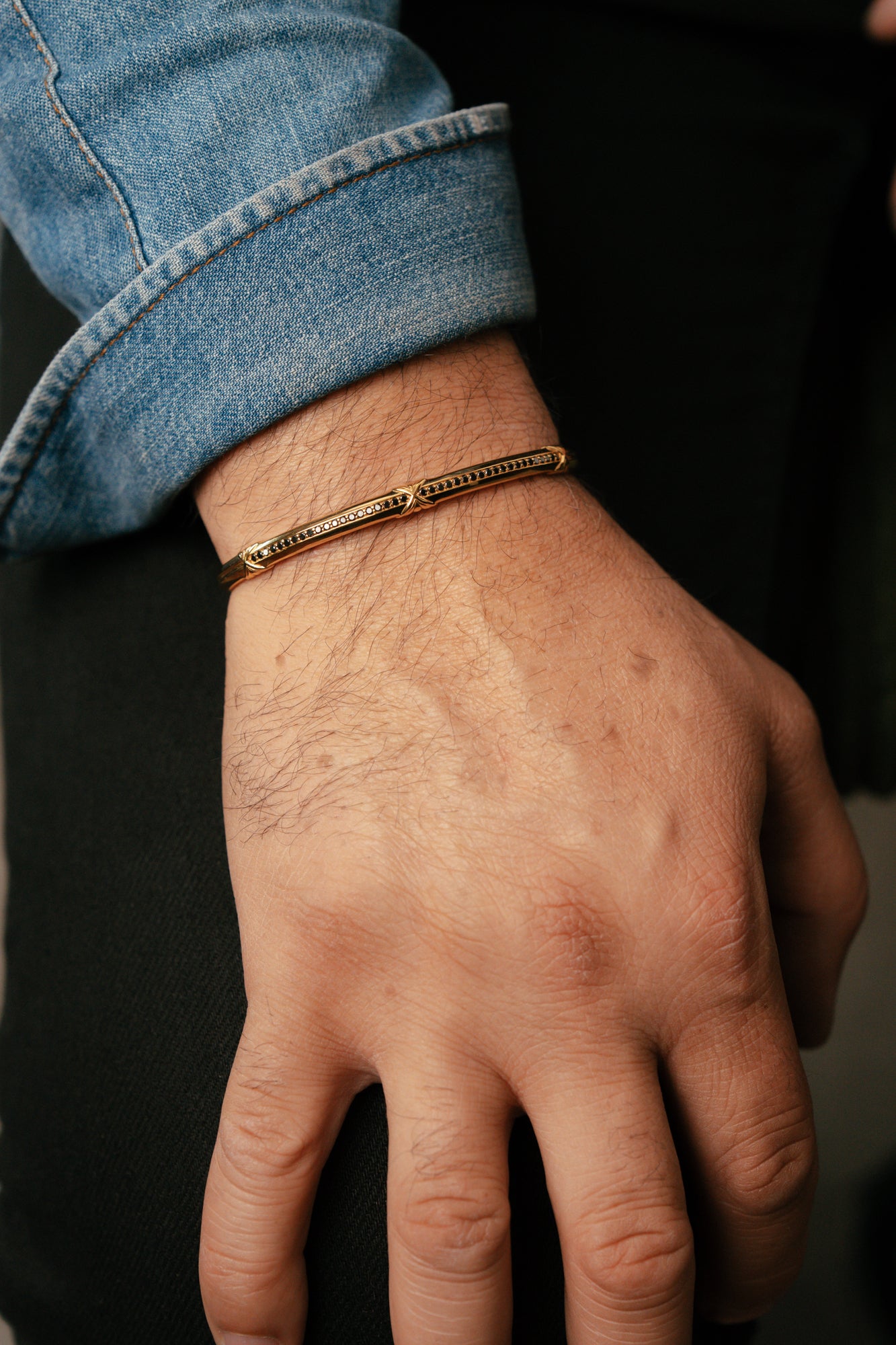 Hand wearing a gold bracelet with a dark background