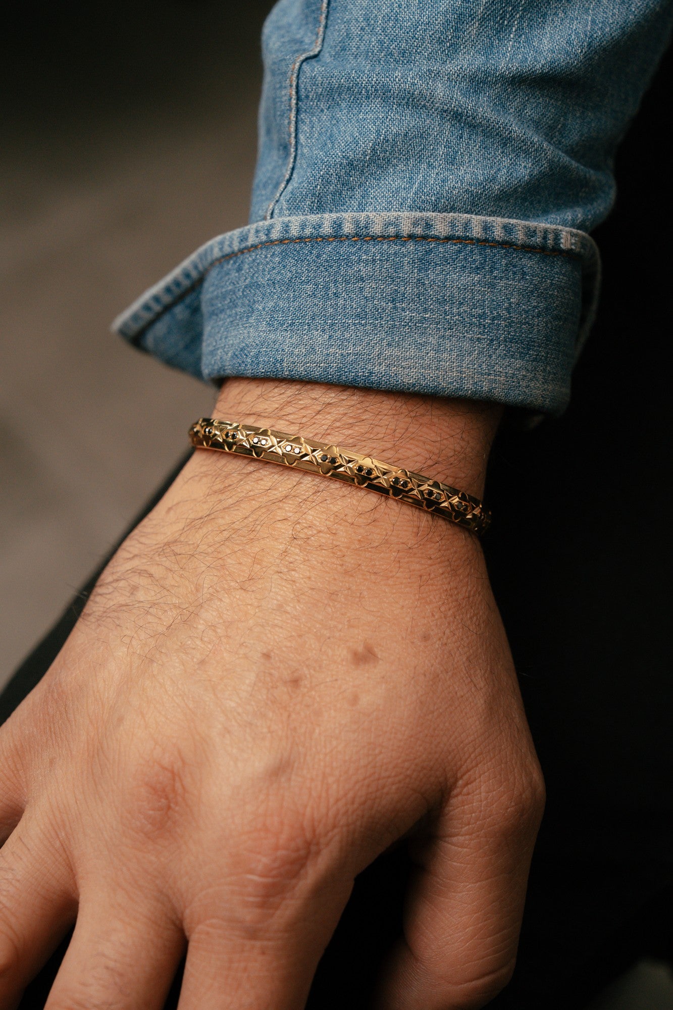 Gold bracelet on a wrist with rolled-up jeans, against a dark background