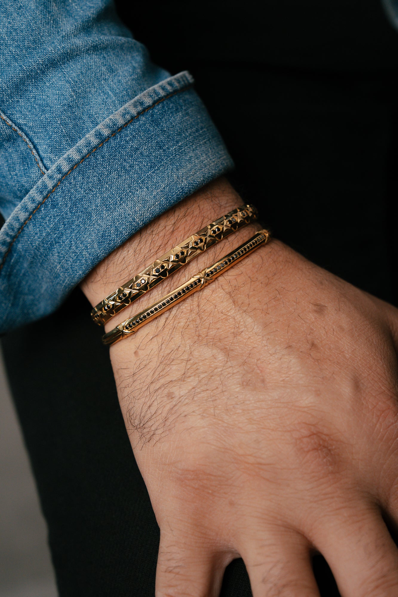 Close-up of a hand wearing two gold bracelets on a dark background