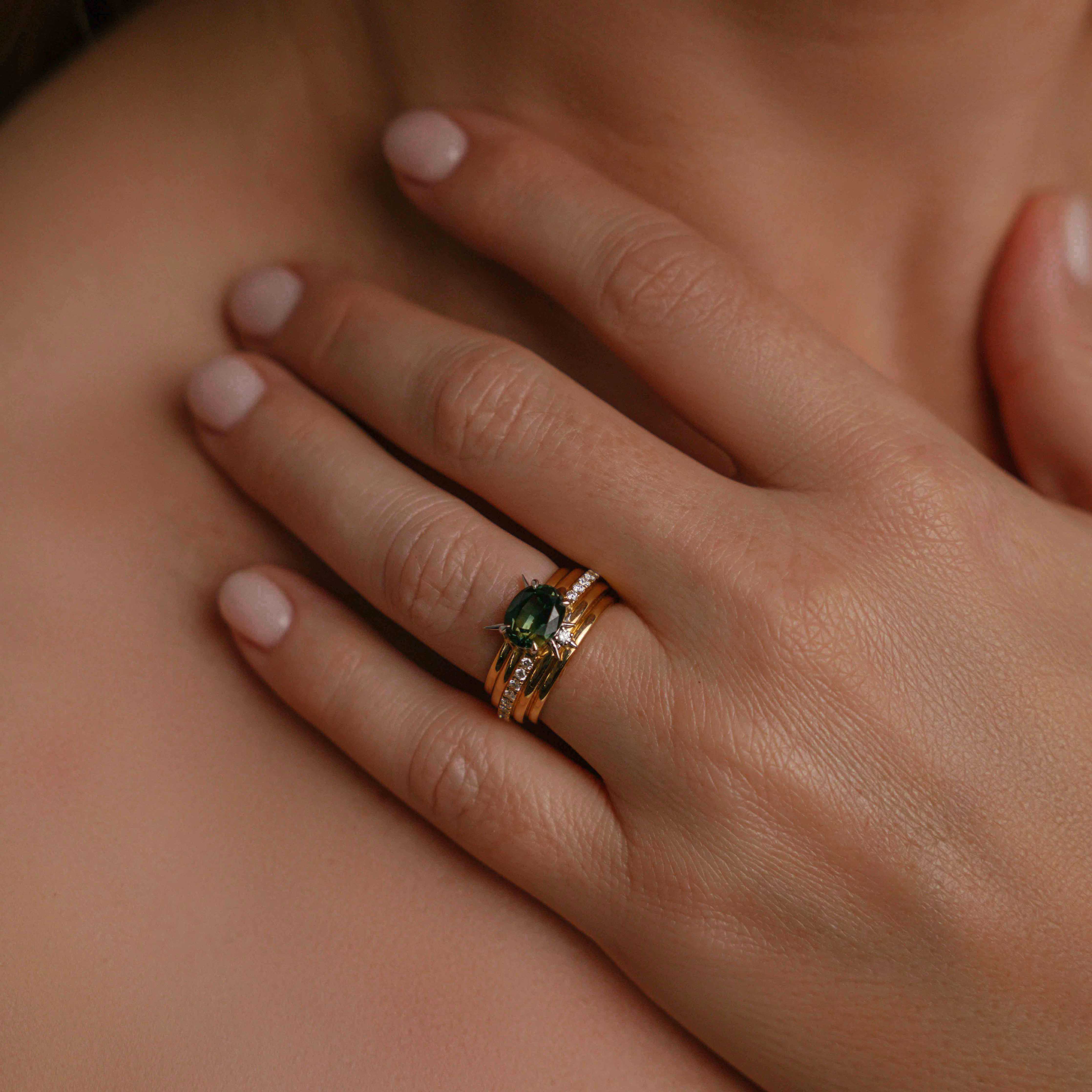 Model wearing ring on engagement ring fingrer,  ring featuring a central dark green oval gemstone, accented by diamond details and pointed silver prongs