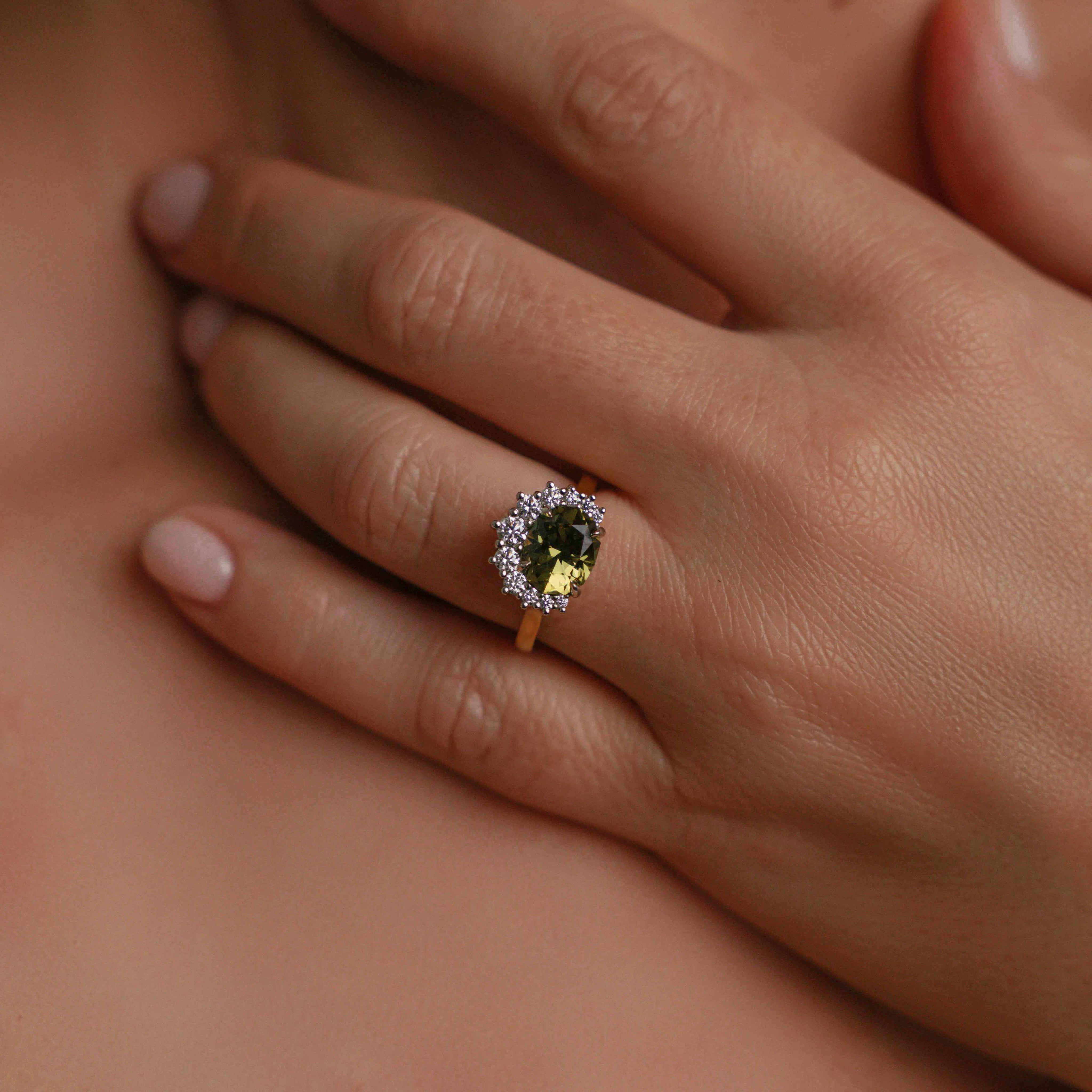 Model wearing ring on engagement finger, of gold ring with a large, cushion-cut dark green Australian sapphire at its center, surrounded by a halo of sparkling diamonds