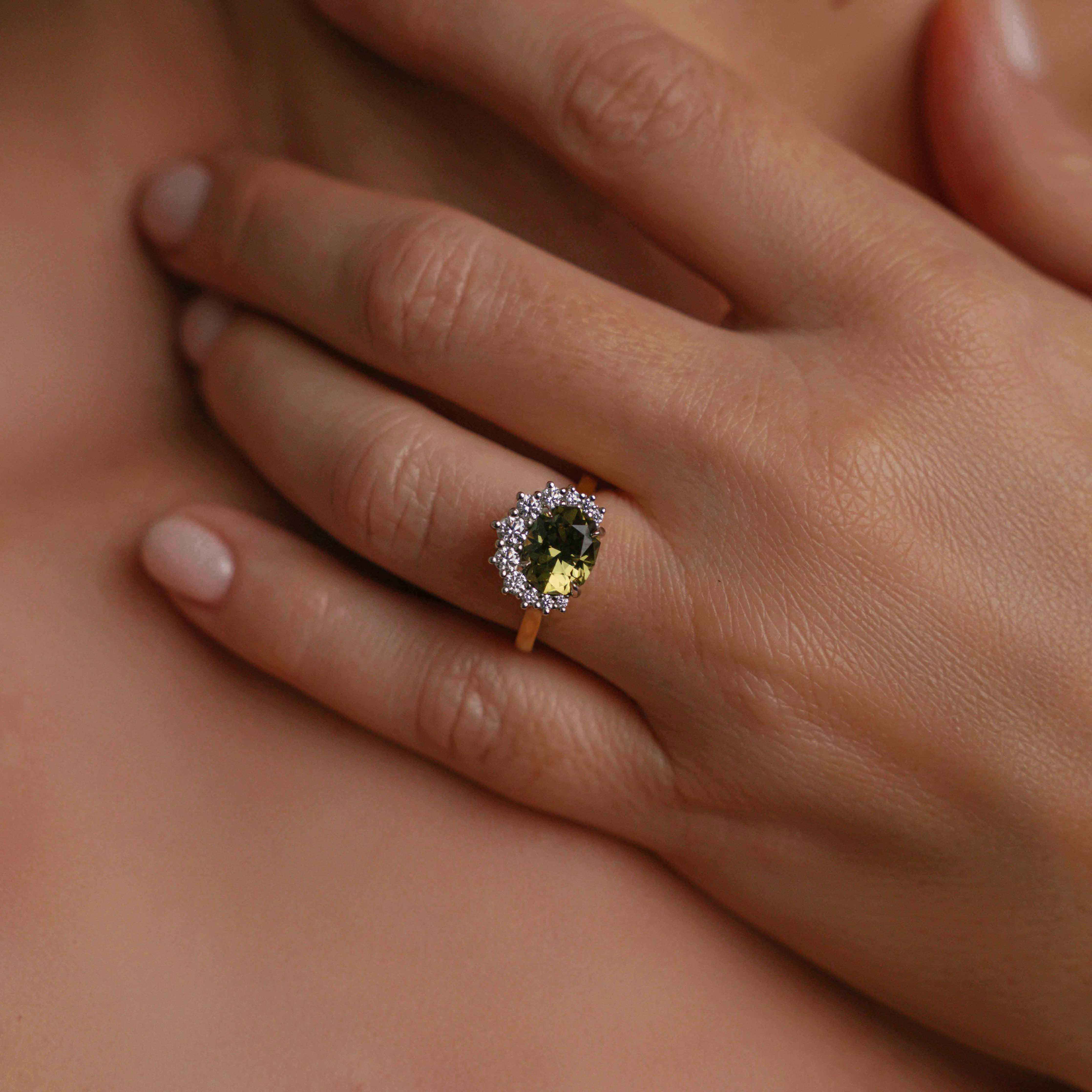 Model wearing ring on engagement finger, of gold ring with a large, cushion-cut dark green Australian sapphire at its center, surrounded by a halo of sparkling diamonds