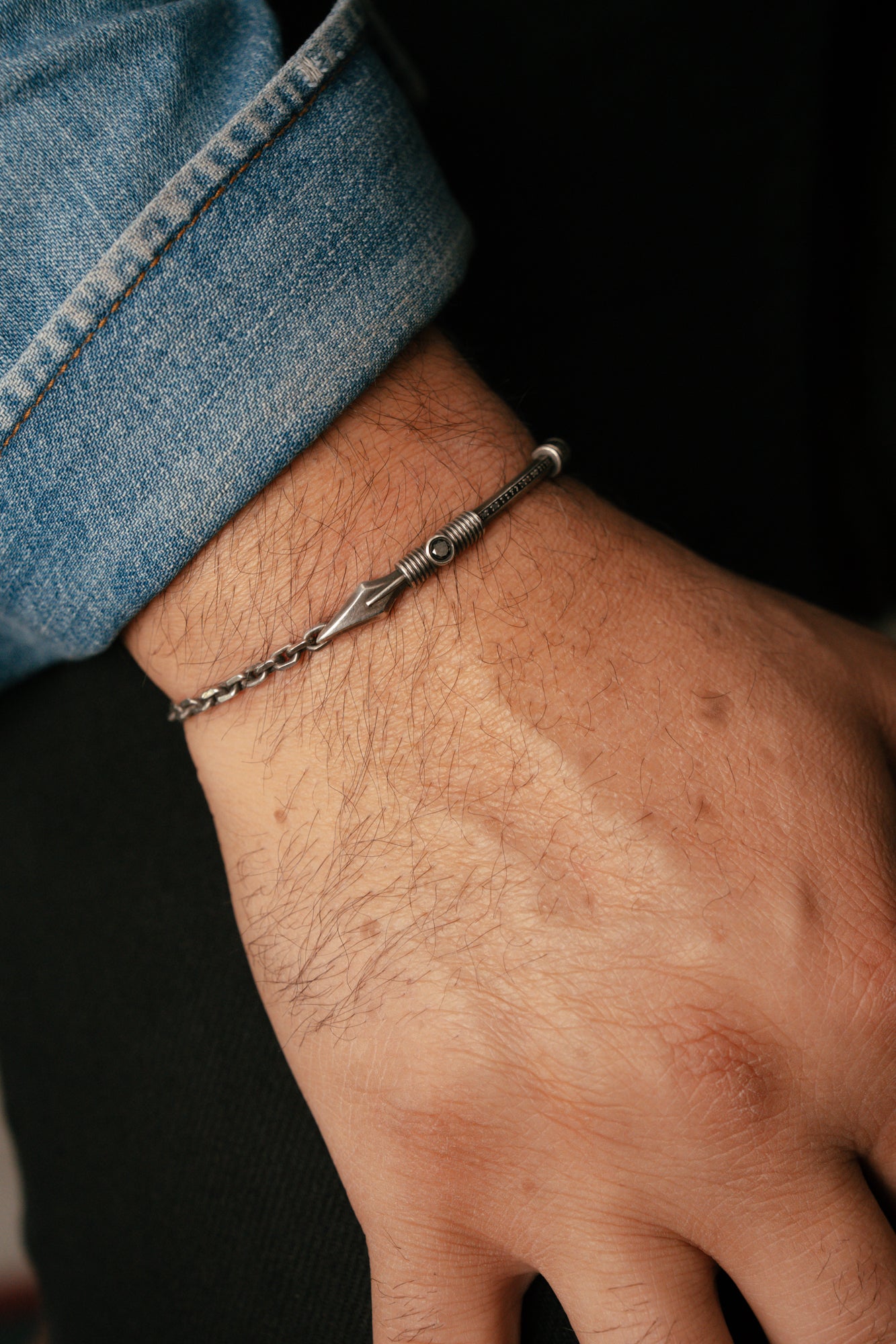 Close-up of a hand wearing a silver bracelet on a dark background