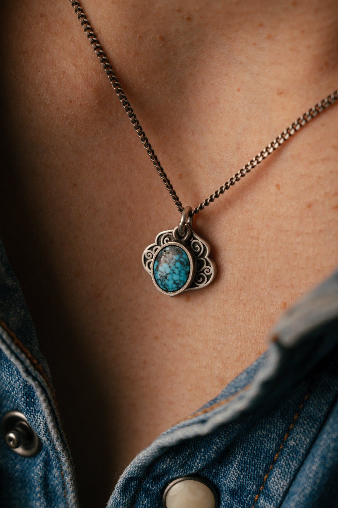 Necklace with a turquoise pendant worn by a person in a denim jacket.