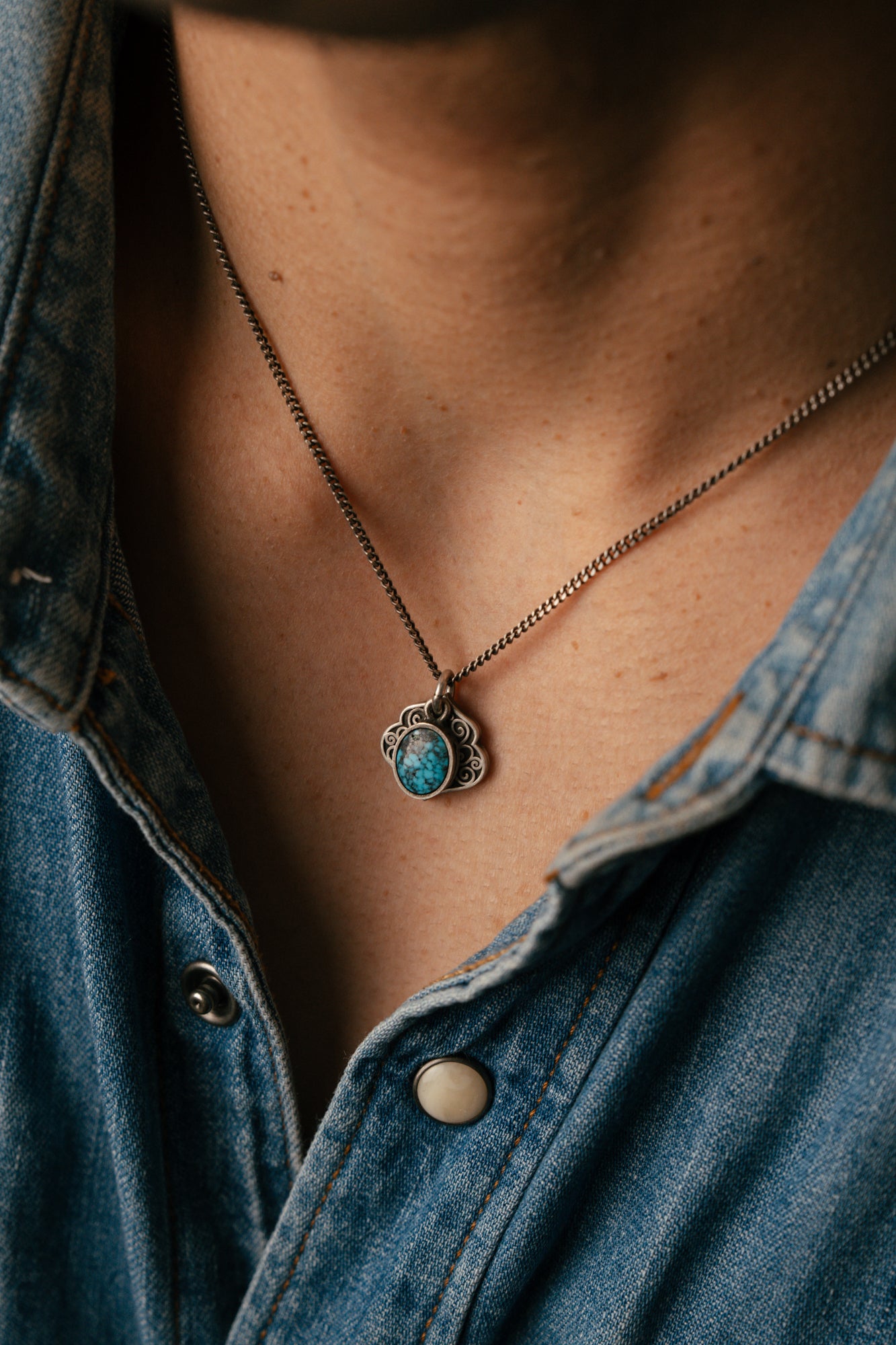 Necklace with a pendant worn by a person wearing a denim shirt.