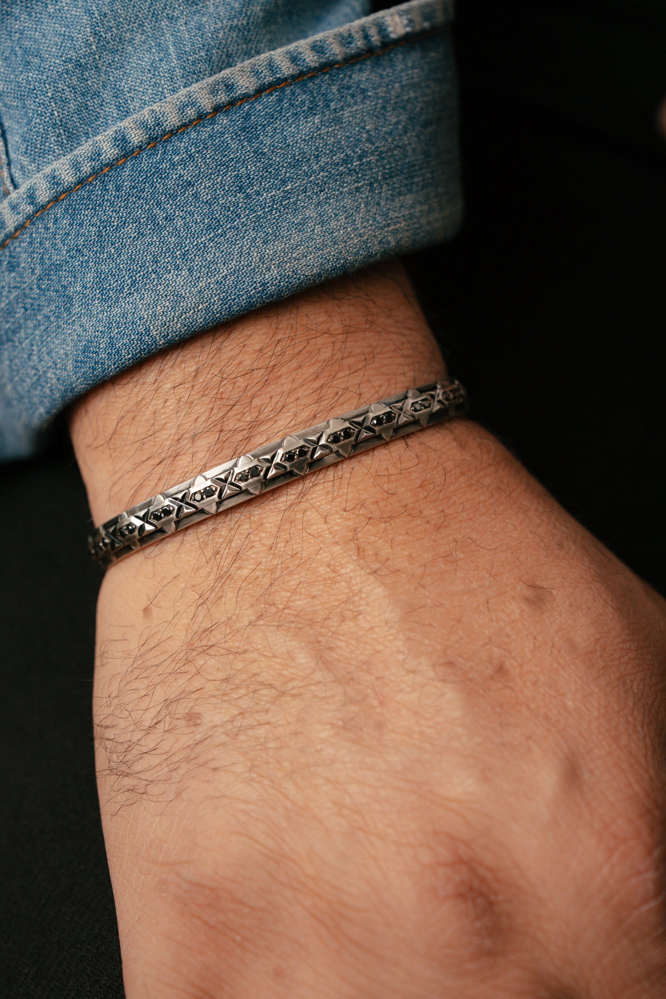 Close-up of a wrist wearing a silver bracelet with a dark background