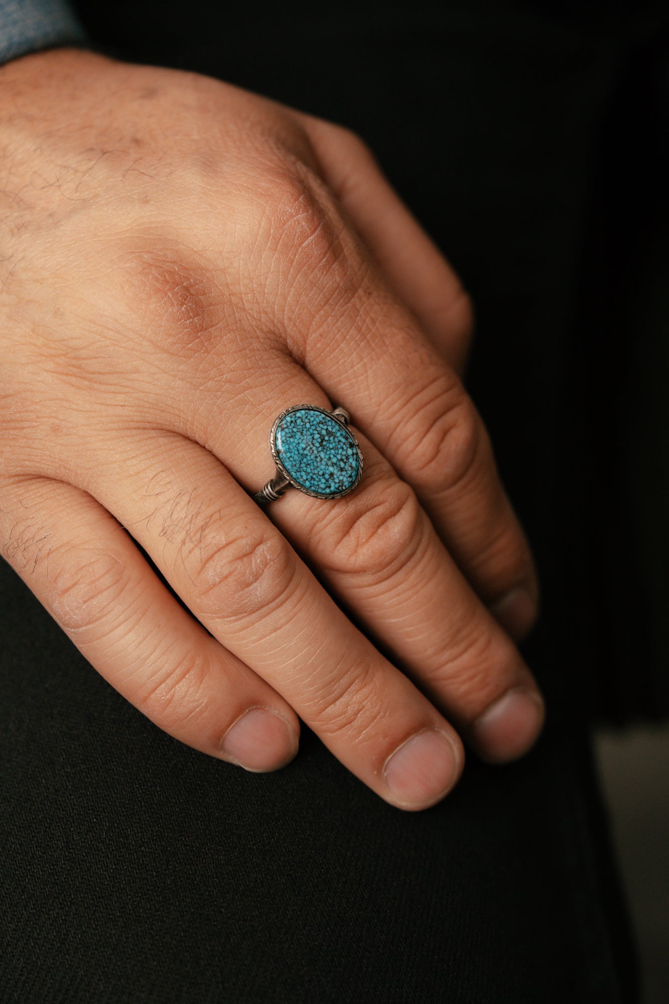 Hand wearing a ring with a blue stone on a dark background