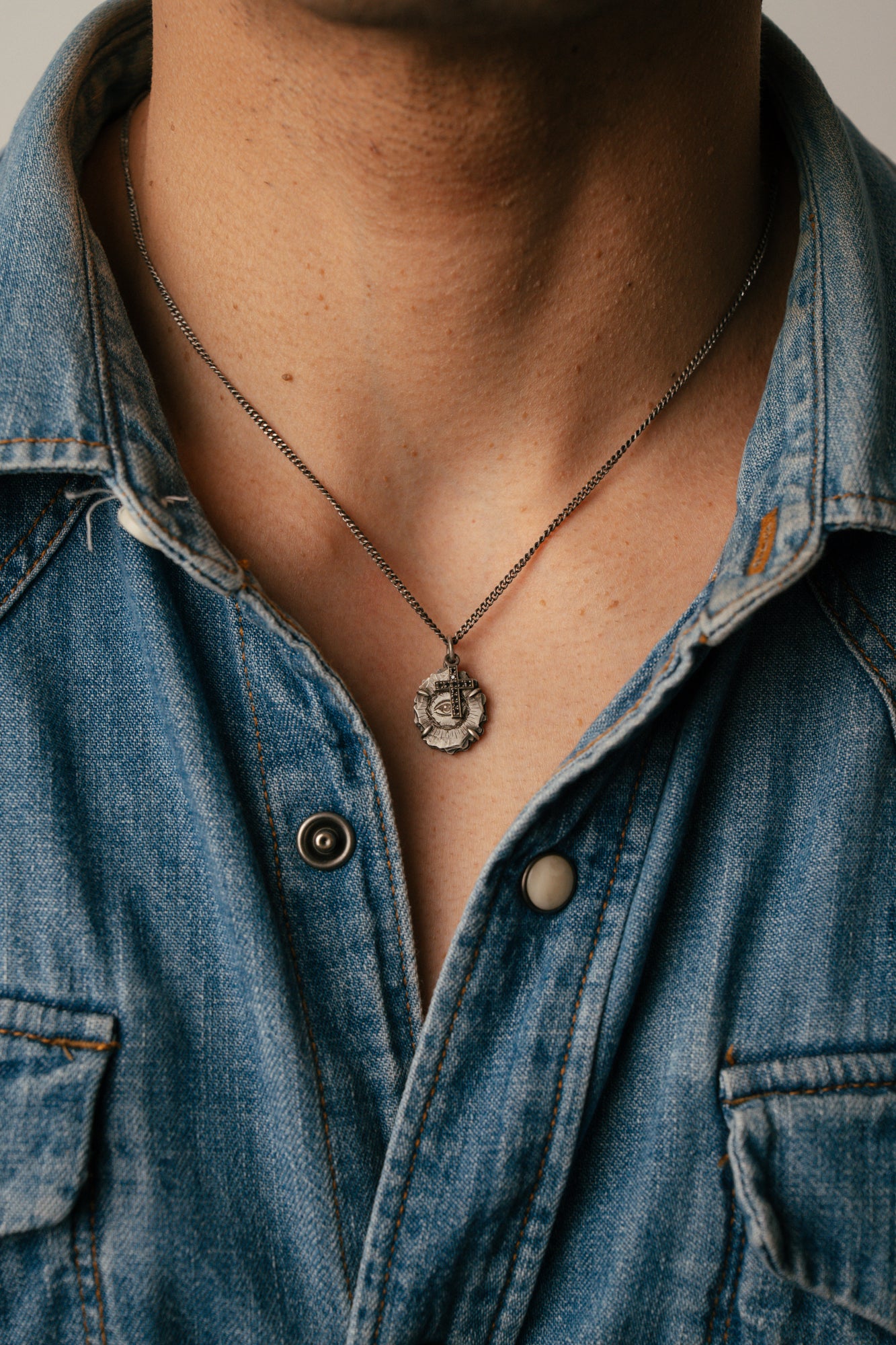 Person wearing a denim shirt with a necklace featuring a pendant.