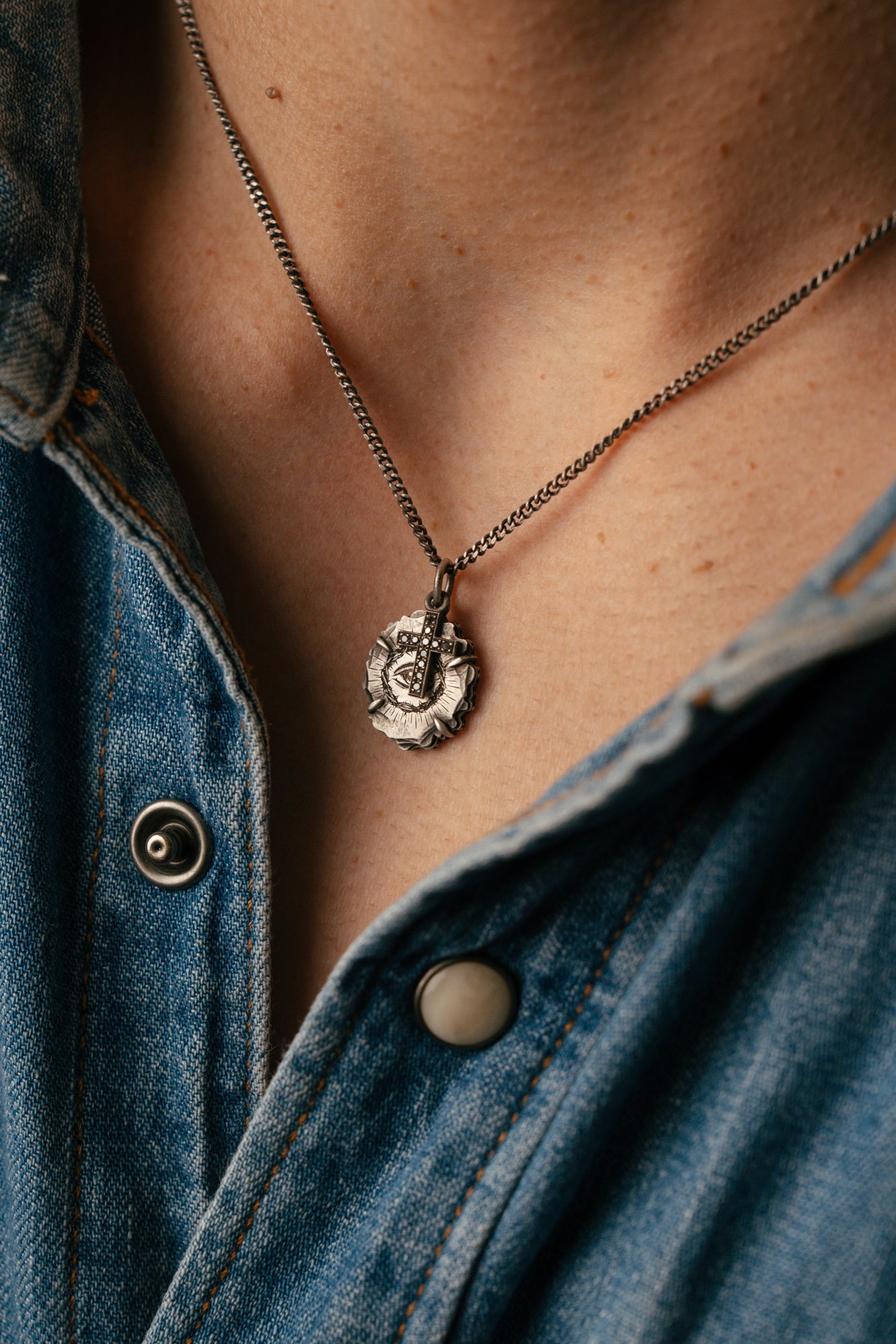 Close-up of a necklace with a pendant worn by a person in a denim shirt.