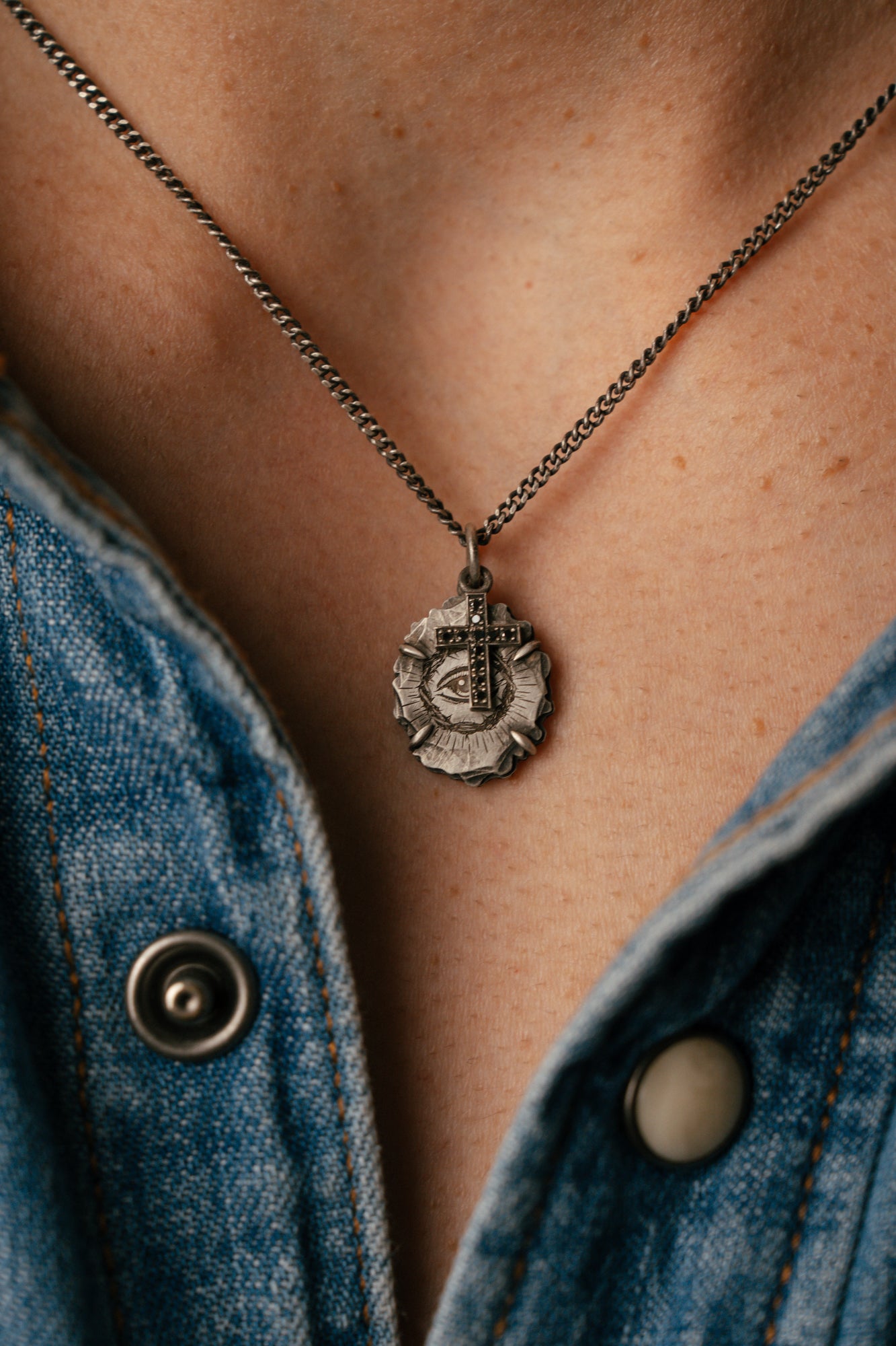 Necklace with a pendant worn by a person wearing a denim jacket.