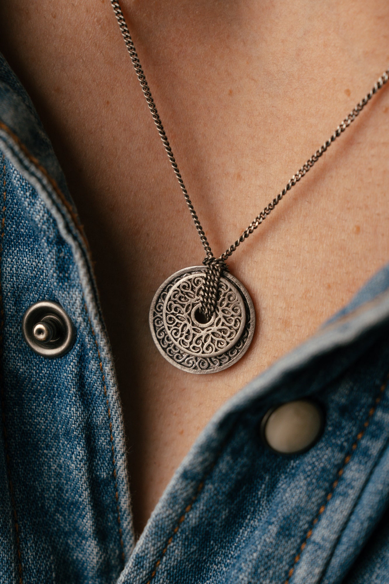 Necklace with a decorative pendant worn by a person wearing a denim jacket.
