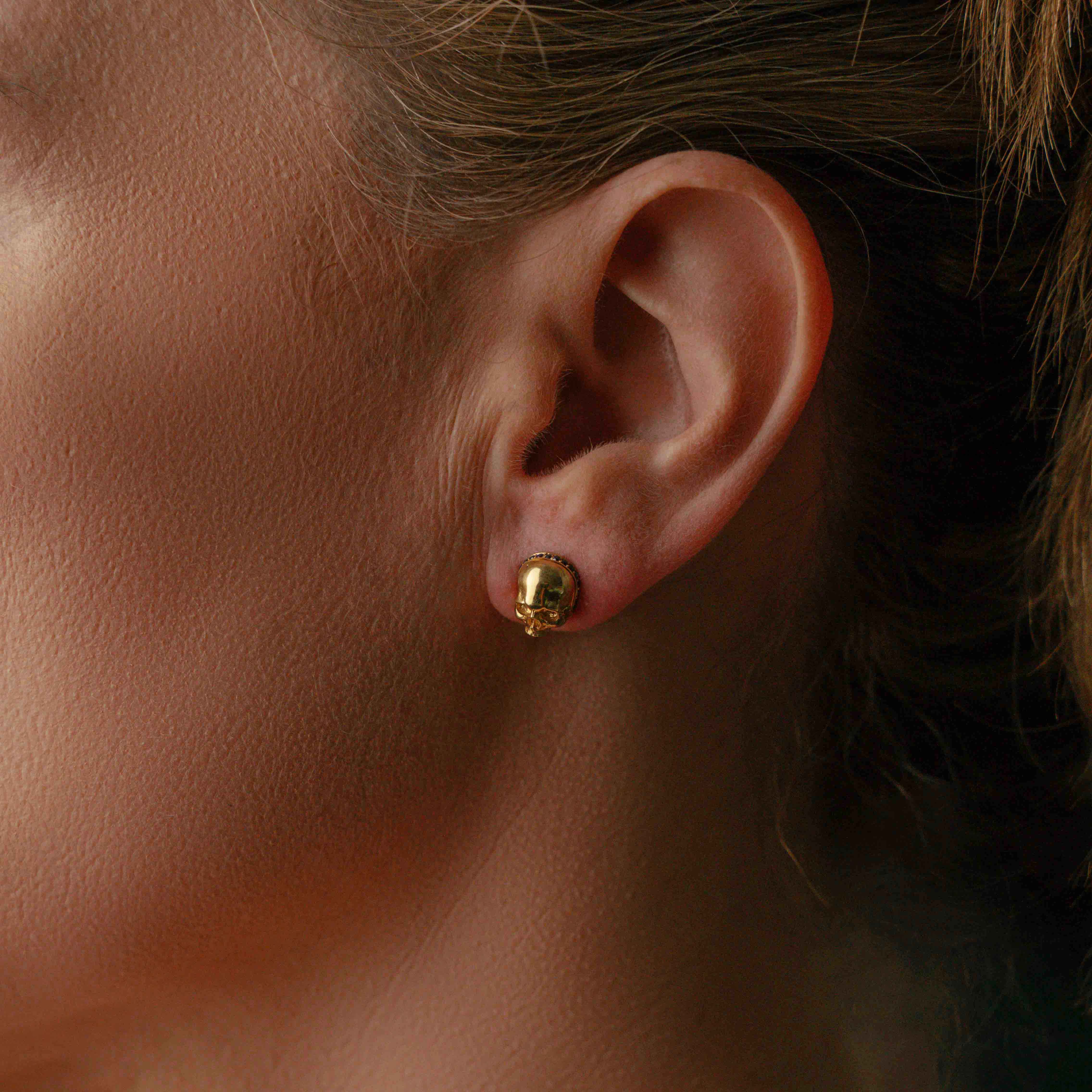 Model wearing Gold skull earrings adorned with black gemstones, featuring a unique, edgy design suitable for a bold fashion statement.