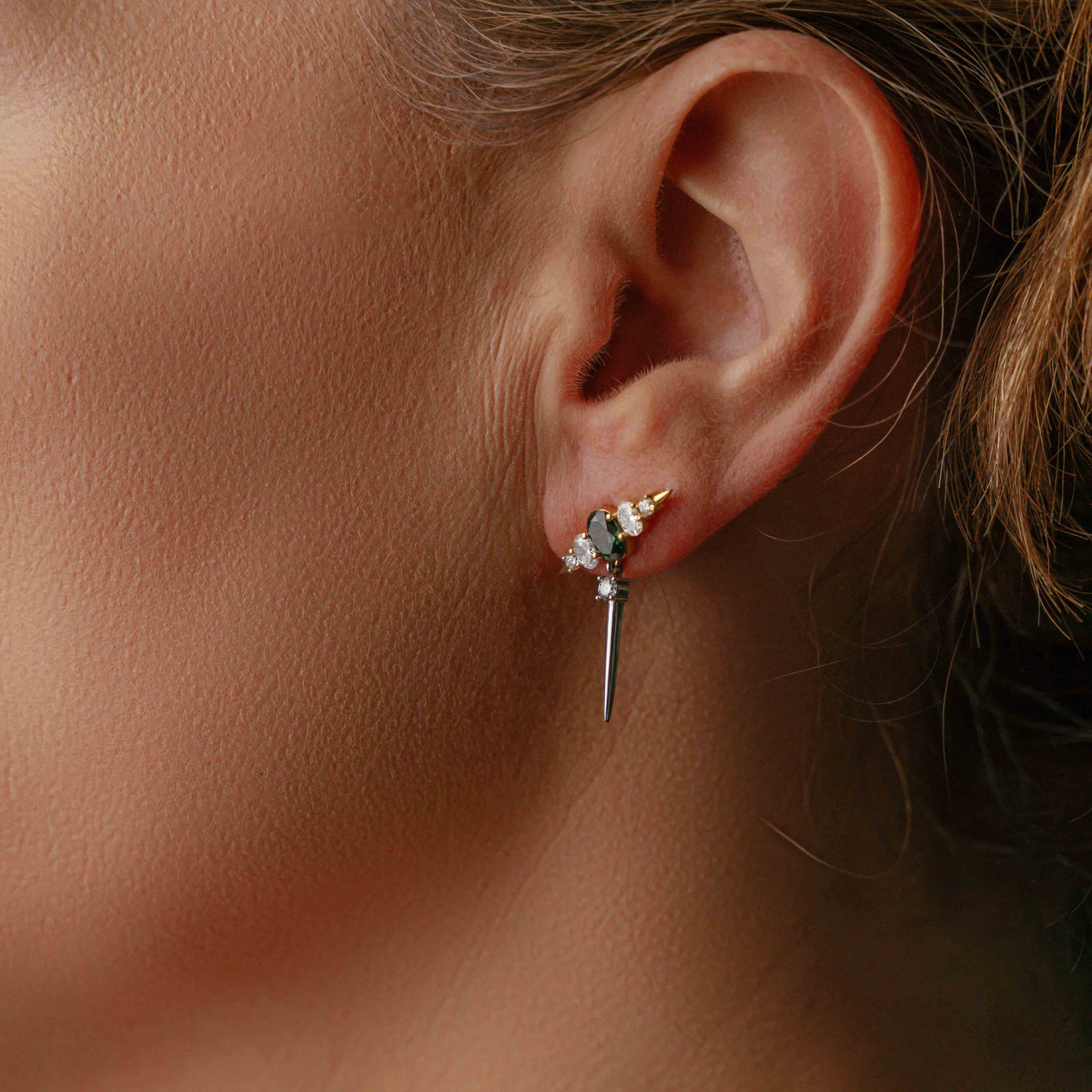Model wearing earring featuring Teal Sapphires, sparkling diamonds, and sleek platinum spikes set in gold accents
