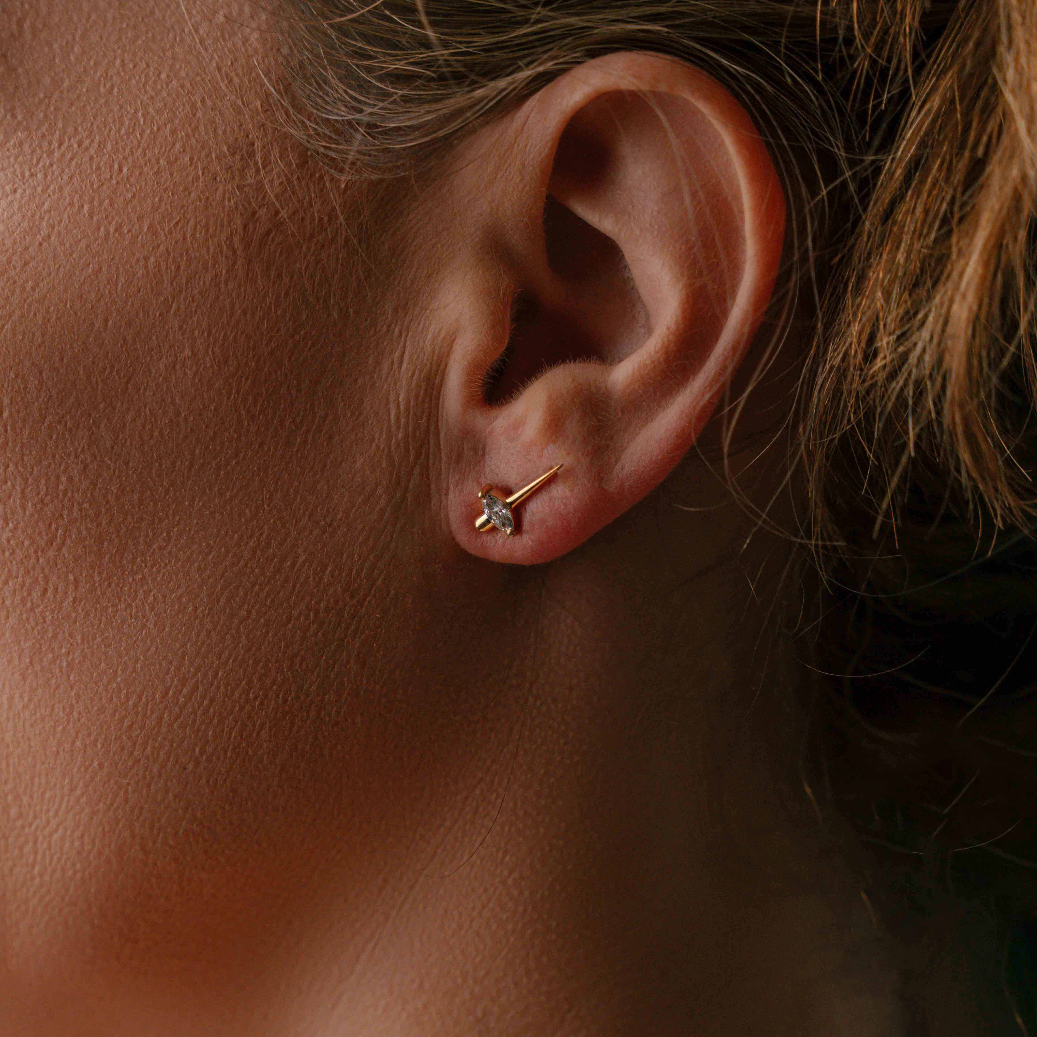 Model wearing gold earrings with a pointed cone design, featuring marquise-cut diamonds set in the center, reflecting light beautifully.