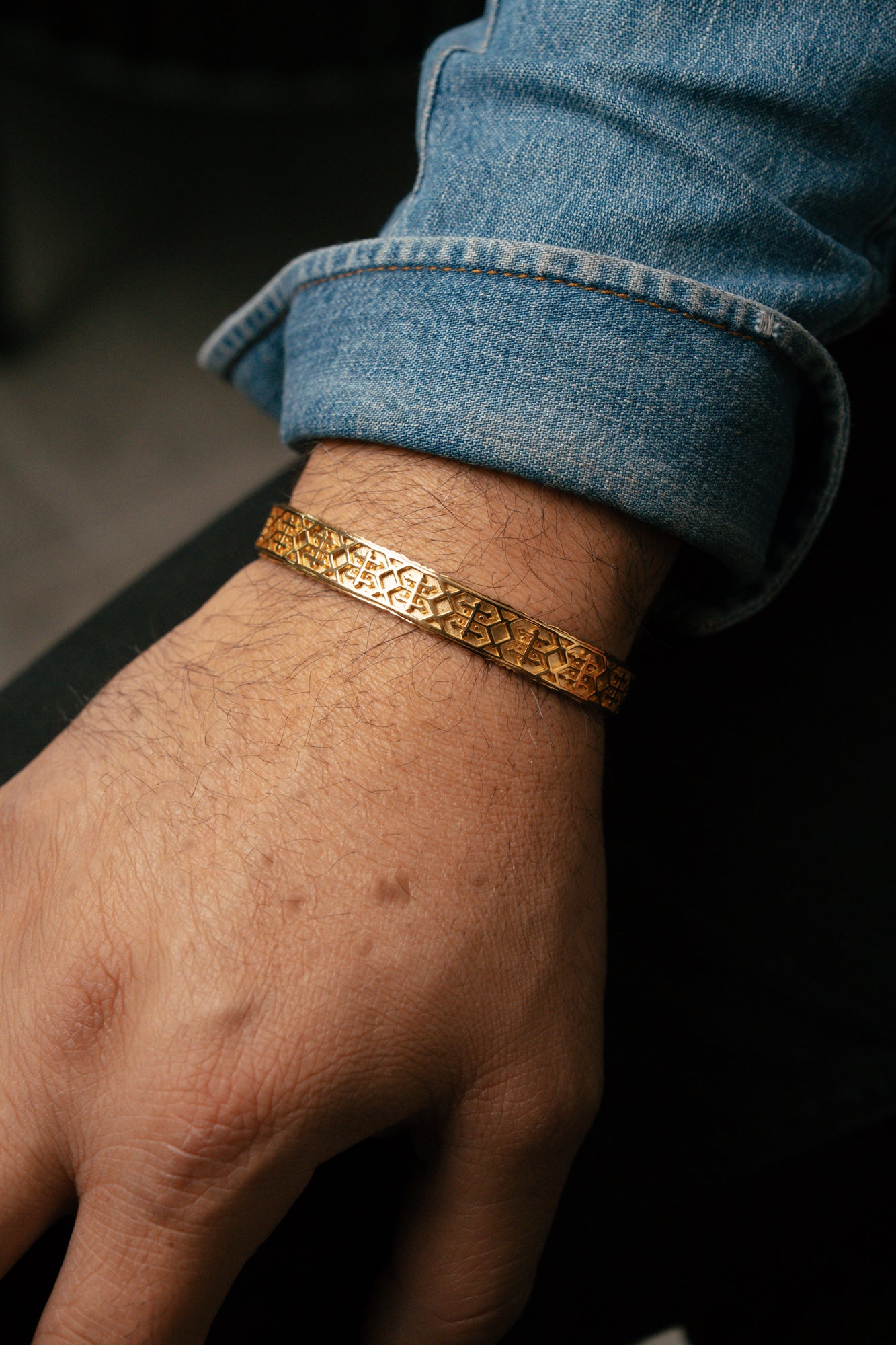 Gold bracelet on a wrist with rolled-up blue jeans