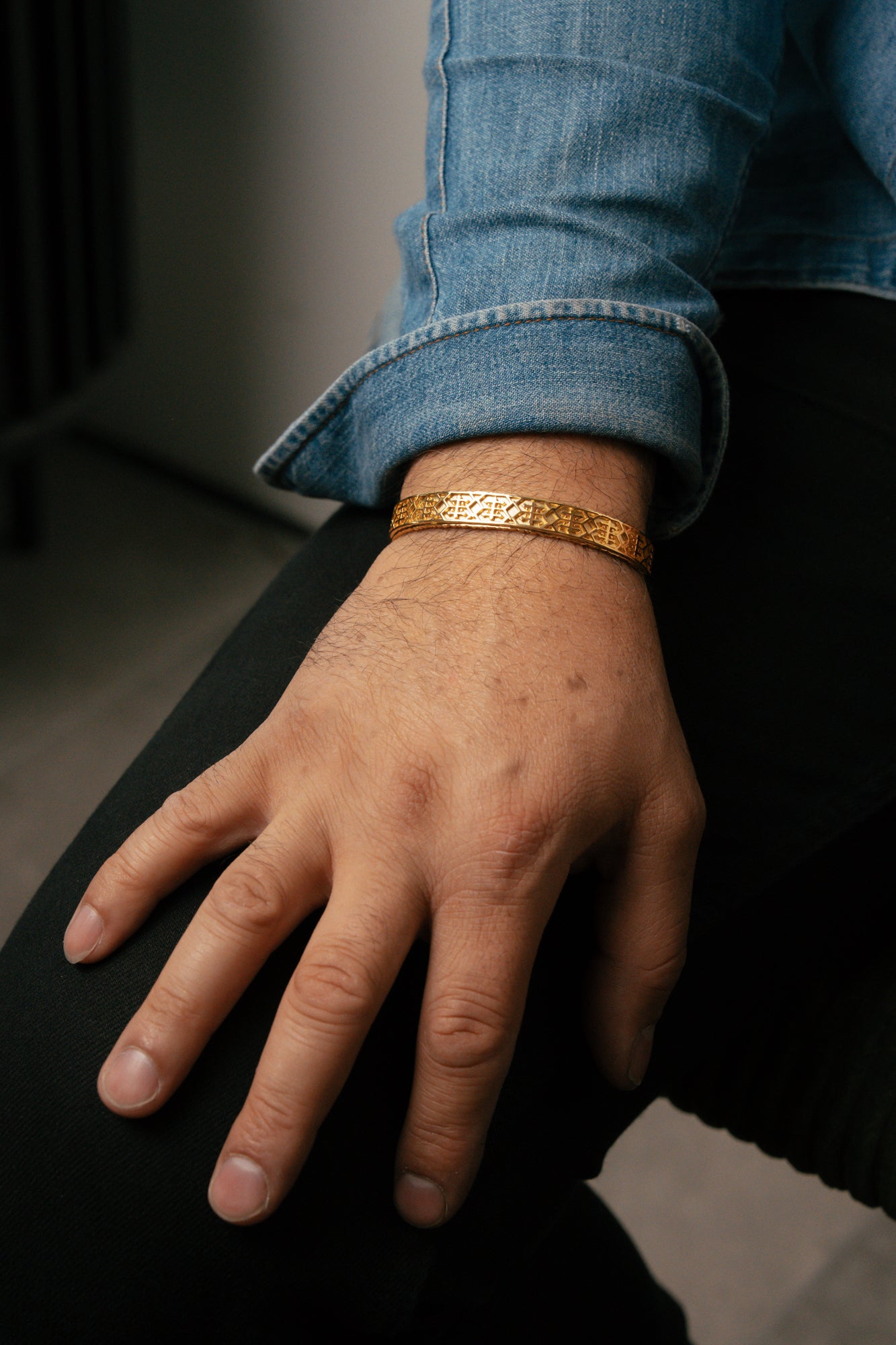 Hand wearing a gold bracelet with rolled-up blue jeans