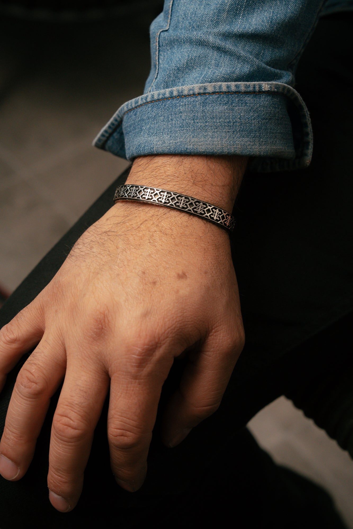 Hand wearing a silver bracelet with a dark background