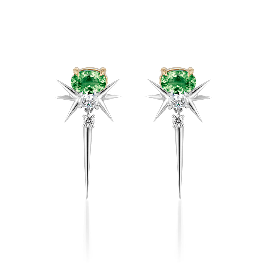 earrings feature a unique design with a central green gemstone—likely a tourmaline or similar stone—set in a gold or light-colored metal prong. The earrings are accented by elongated, pointed spikes that create a starburst effect, enhancing their dramatic look. The combination of colored stones and metallic elements makes them stand out as a statement piece.