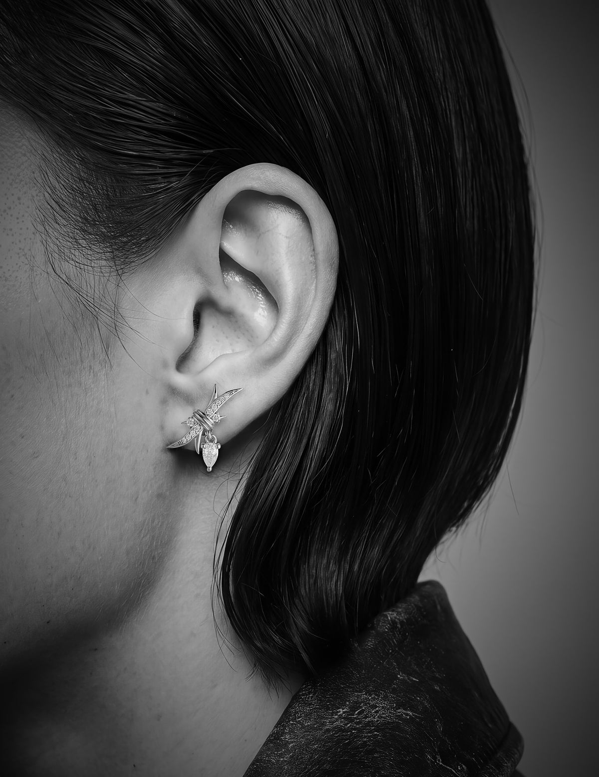A close-up black and white photograph of a person's ear wearing a delicate, starburst-shaped stud earring with small clear stones.