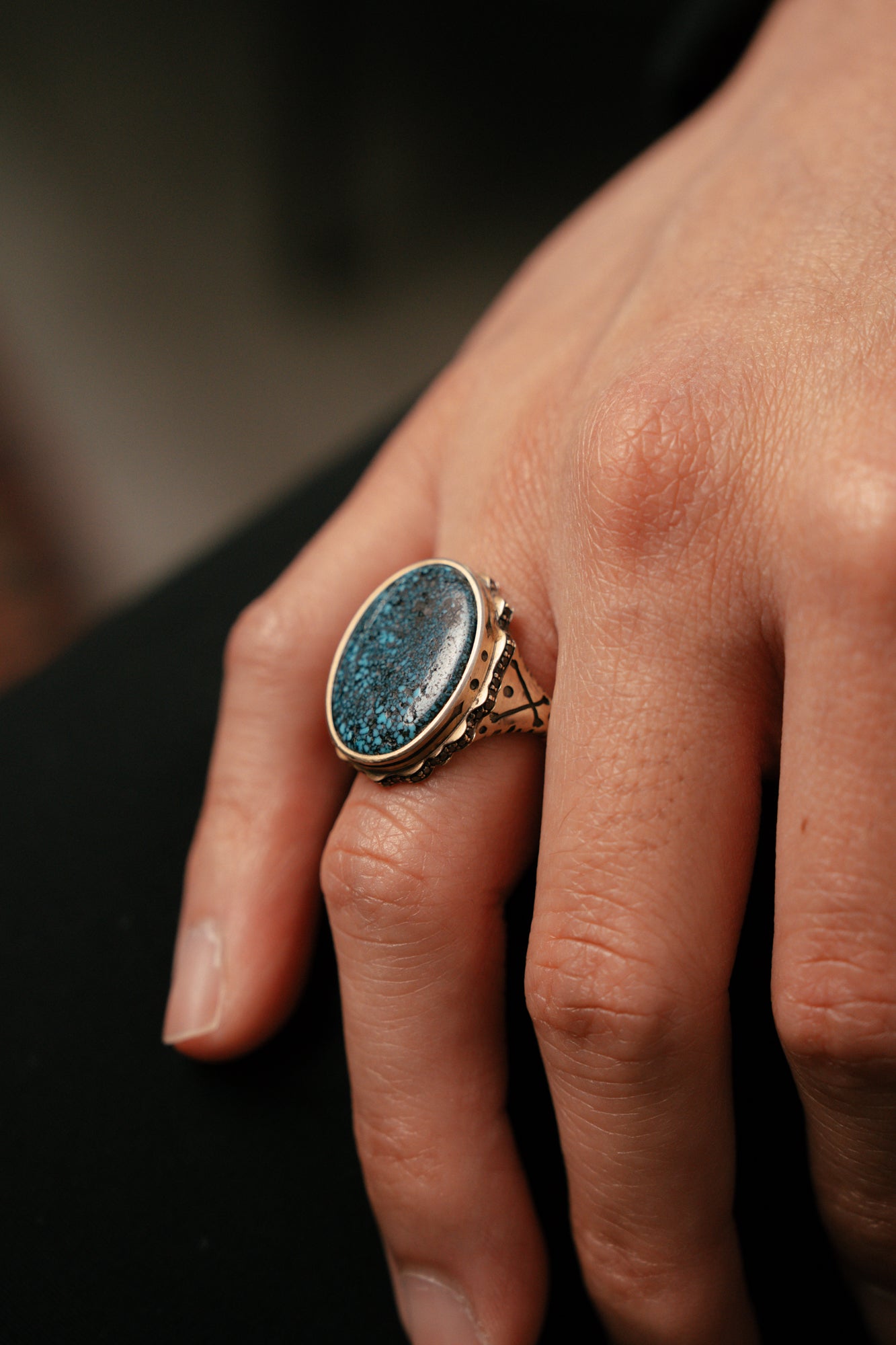 Close-up of a hand wearing a ring with a blue stone on a blurred background