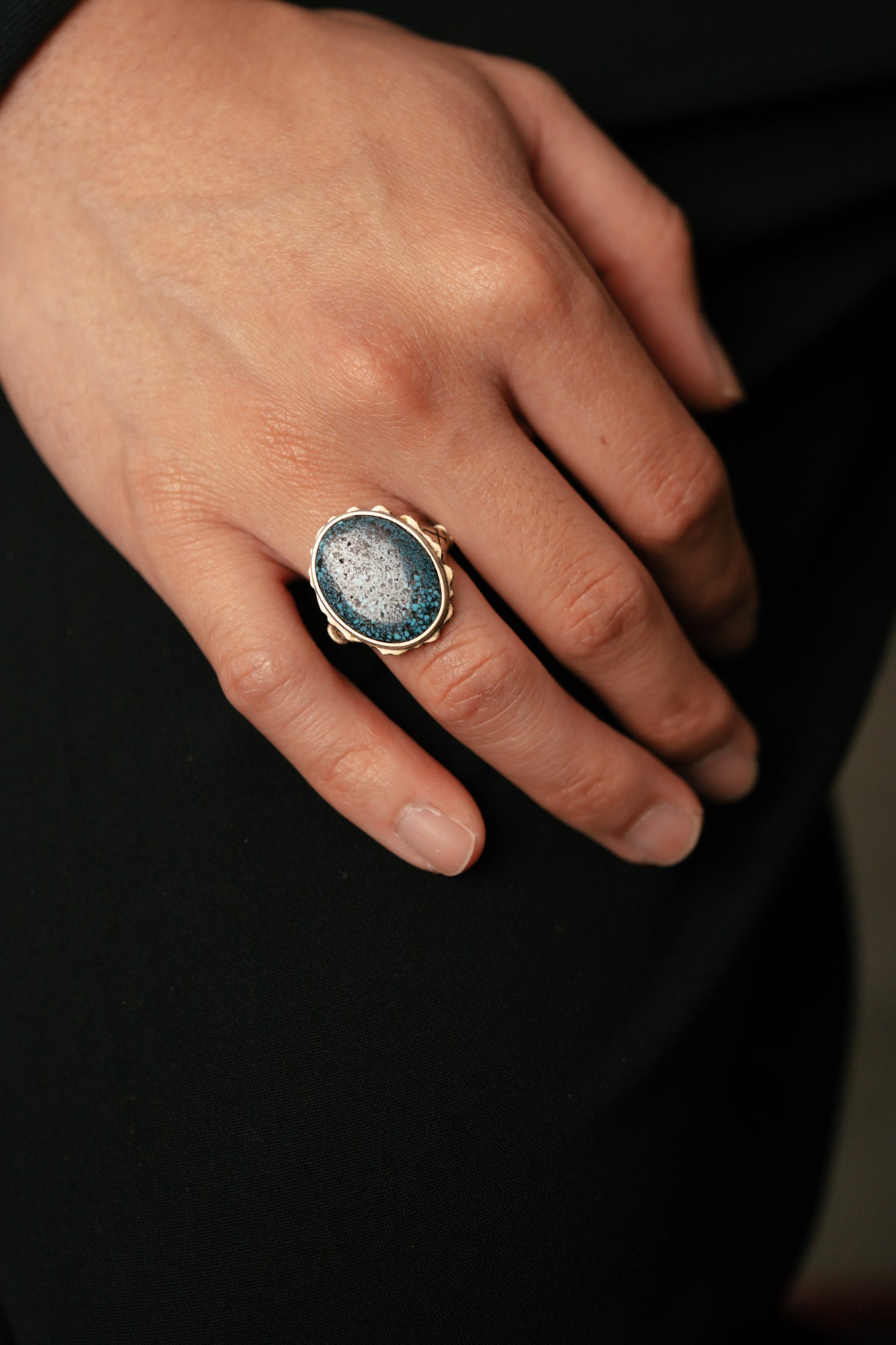 Close-up of a hand wearing a ring with a blue gemstone on a dark background