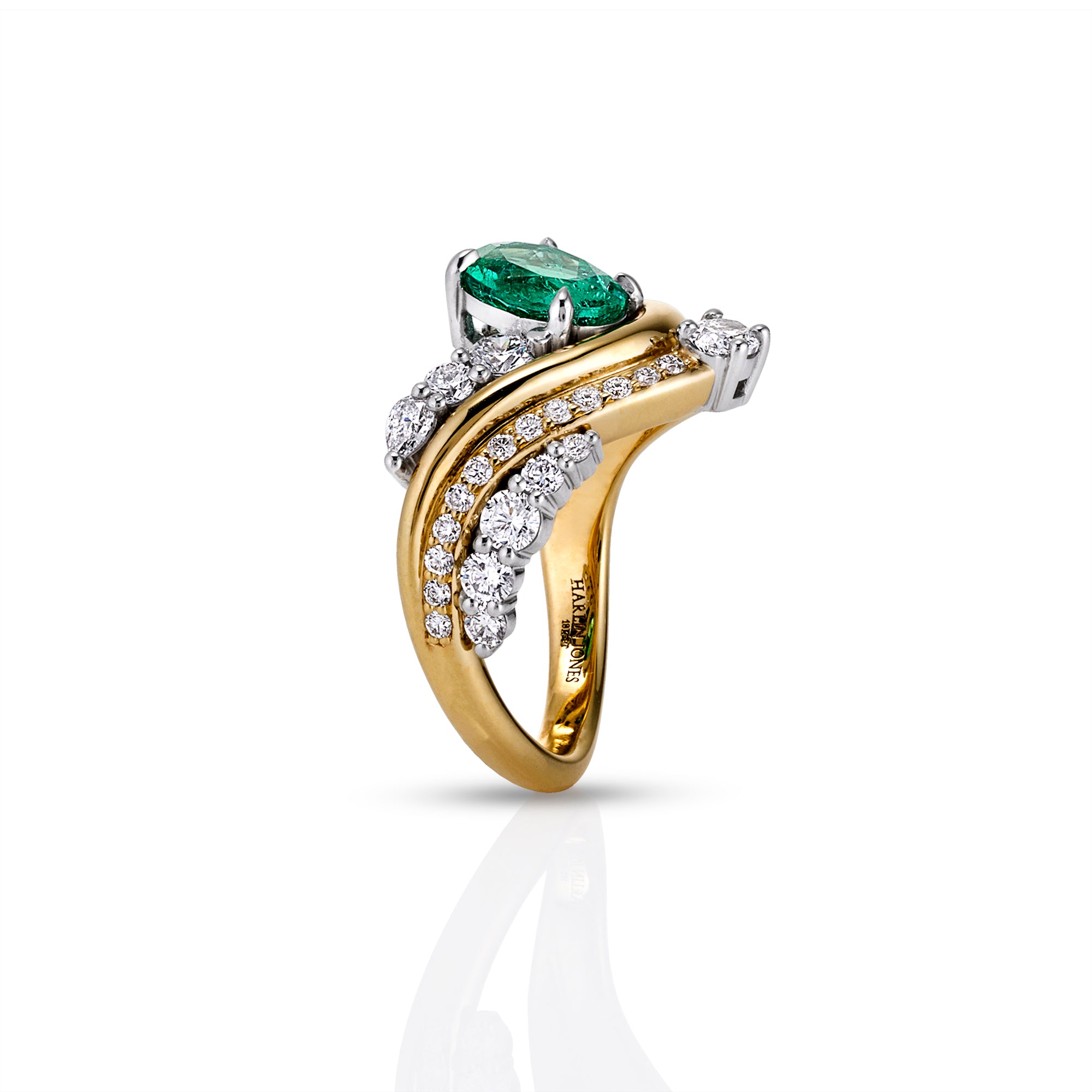 A two-tone yellow and white gold ring featuring a cushion-cut green emerald center stone and pavé-set round diamonds along curved bands, shown on a white background with a soft reflection.