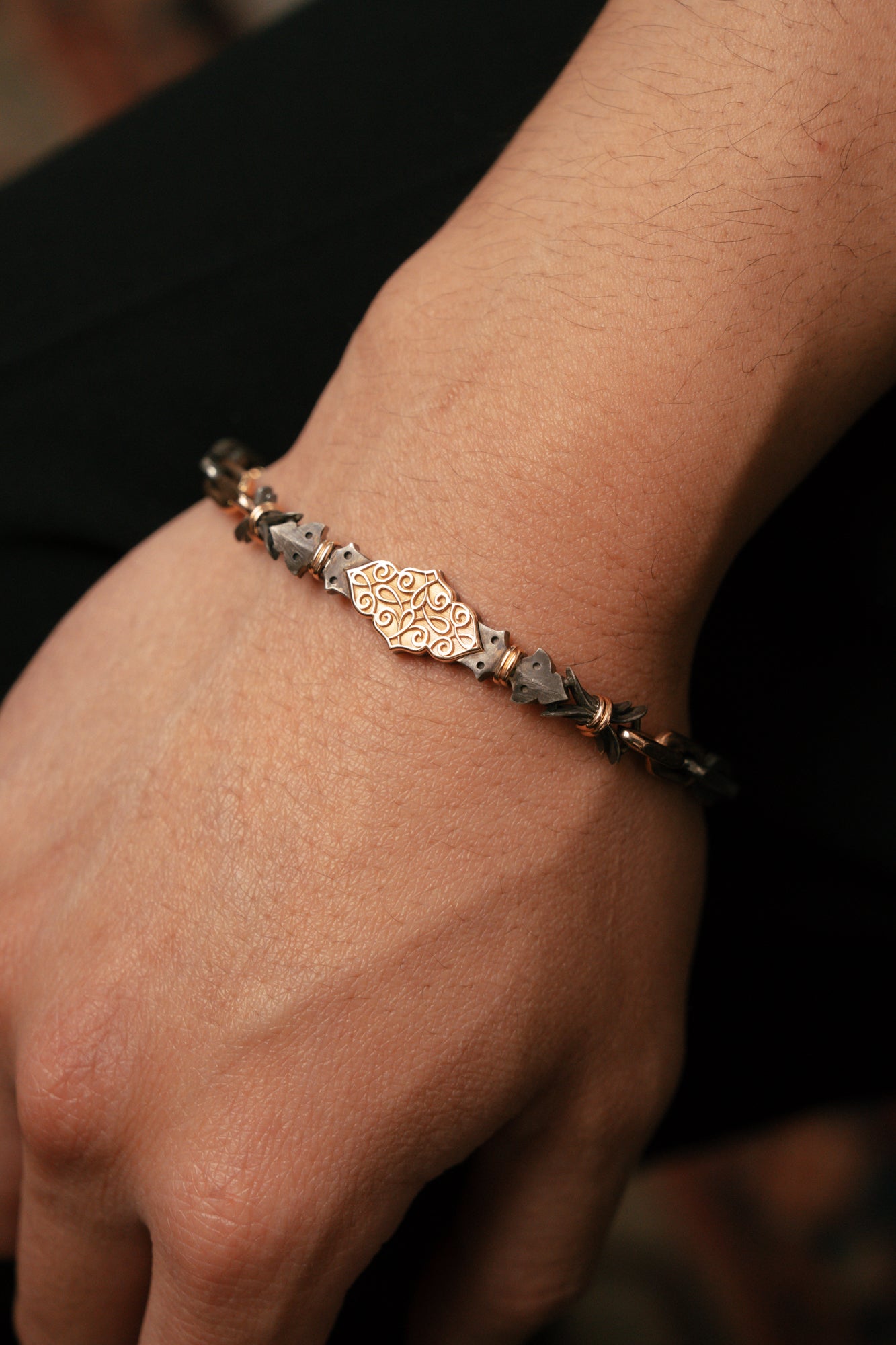 Close-up of a hand wearing a detailed bracelet on a dark background