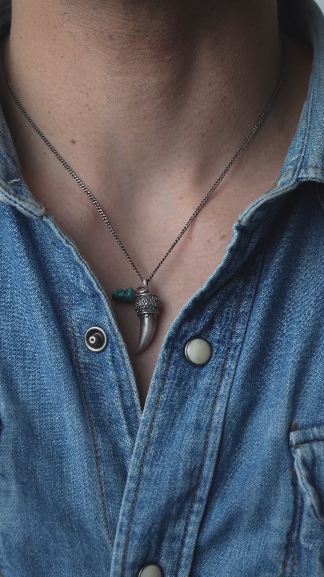 Video person wearing a denim shirt with a necklace featuring a tusk pendant.