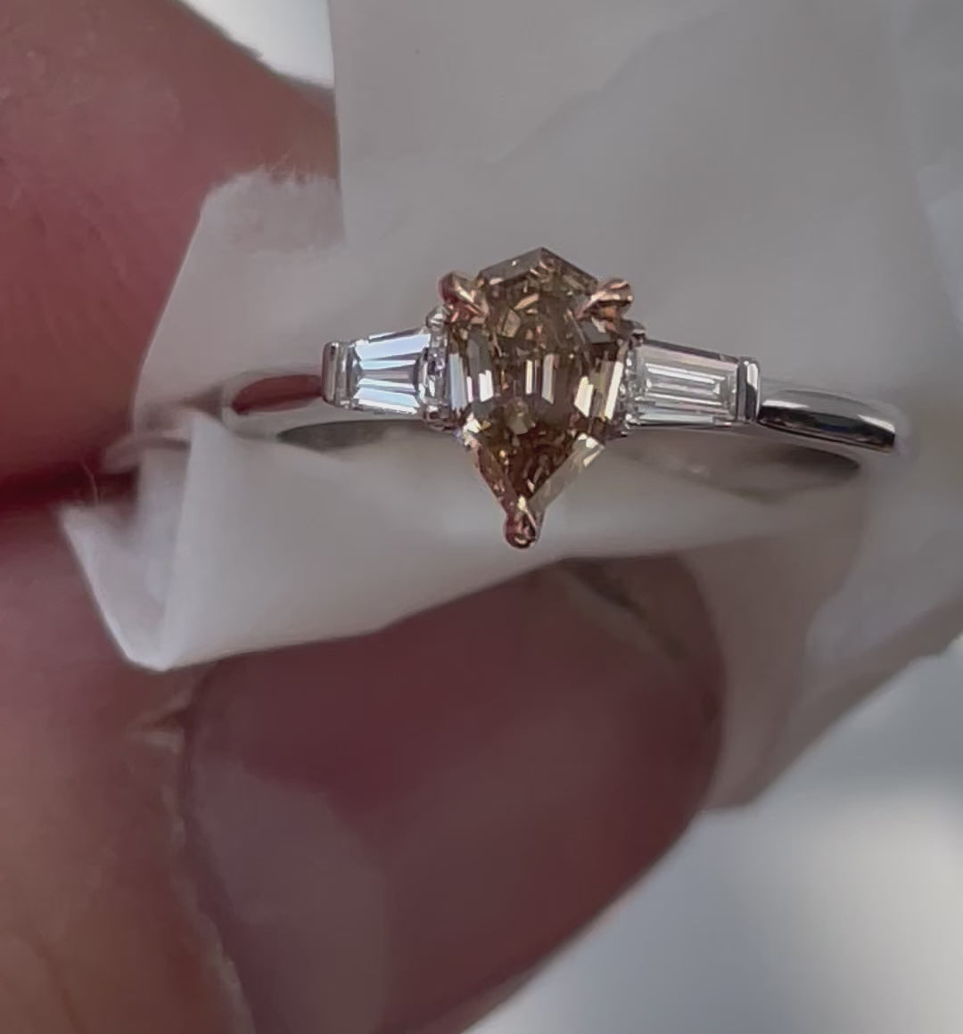 Video of white gold ring with a pear-shaped champagne diamond flanked by two baguette-cut diamonds wrapped in white paper