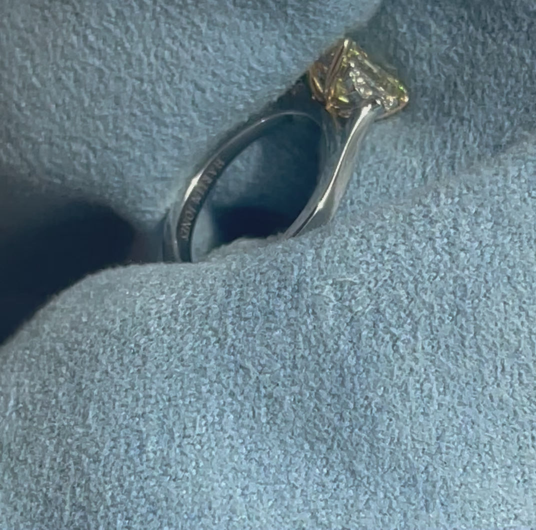 Video of An elegant ring with a central yellow diamond flanked by two smaller clear diamonds moving around on blue cloth 