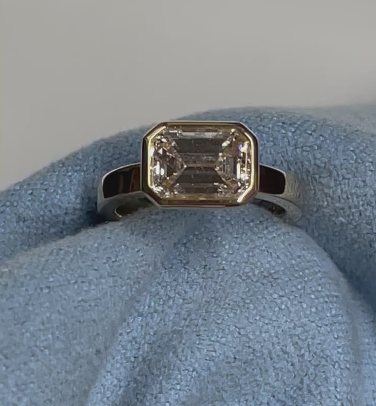 Video Of gold ring with a single emerald cut diamond, moving around on a blue cloth.
